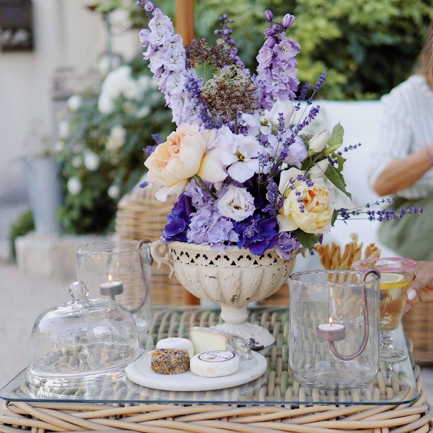 Boeket paarse en crèmekleurige bloemen in witte keramische vaas op glazen tafel met kaarsen en kaasplank