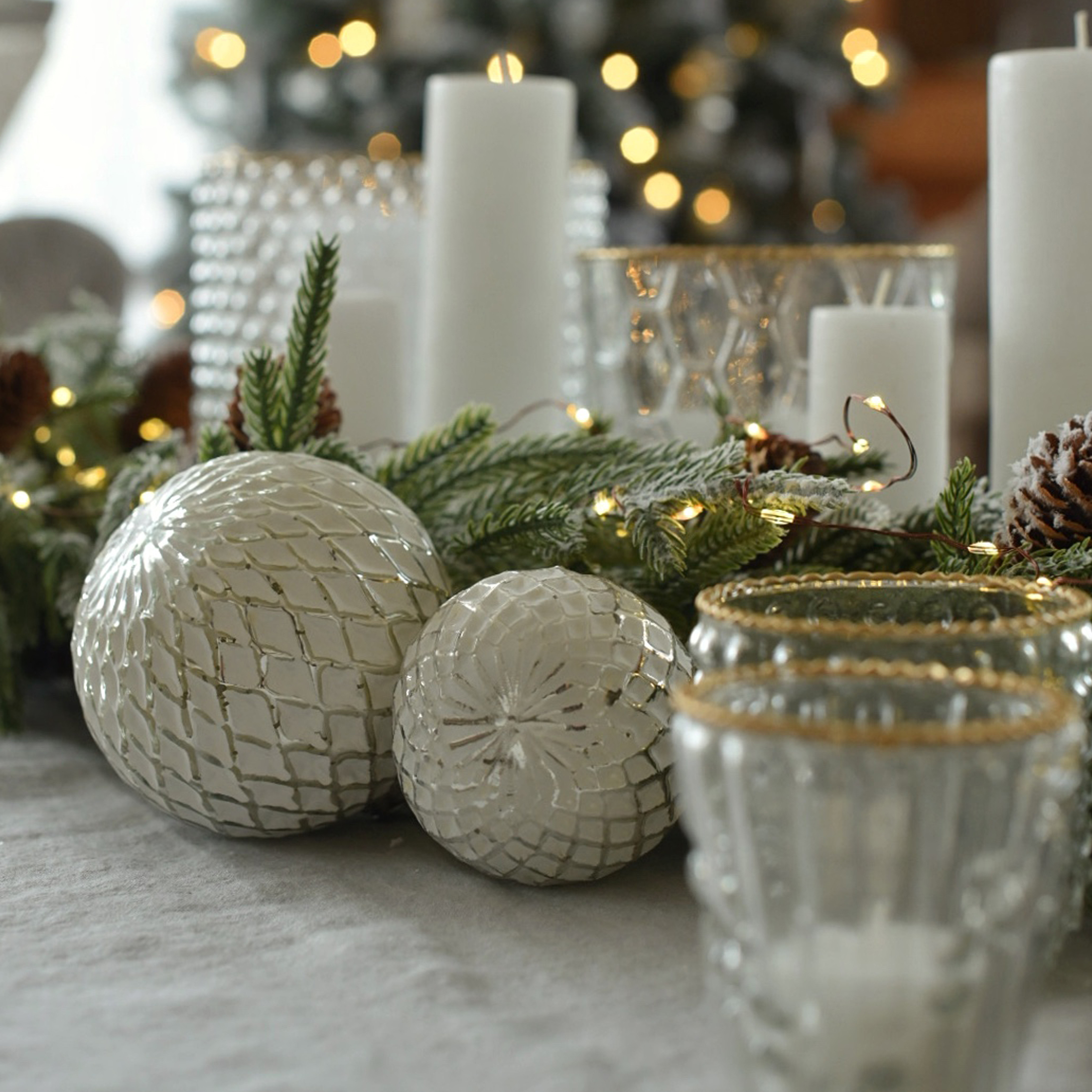 Witte decoratieve glazen ballen met ruitpatroon op feestelijke tafel met groene takken en kaarsen
