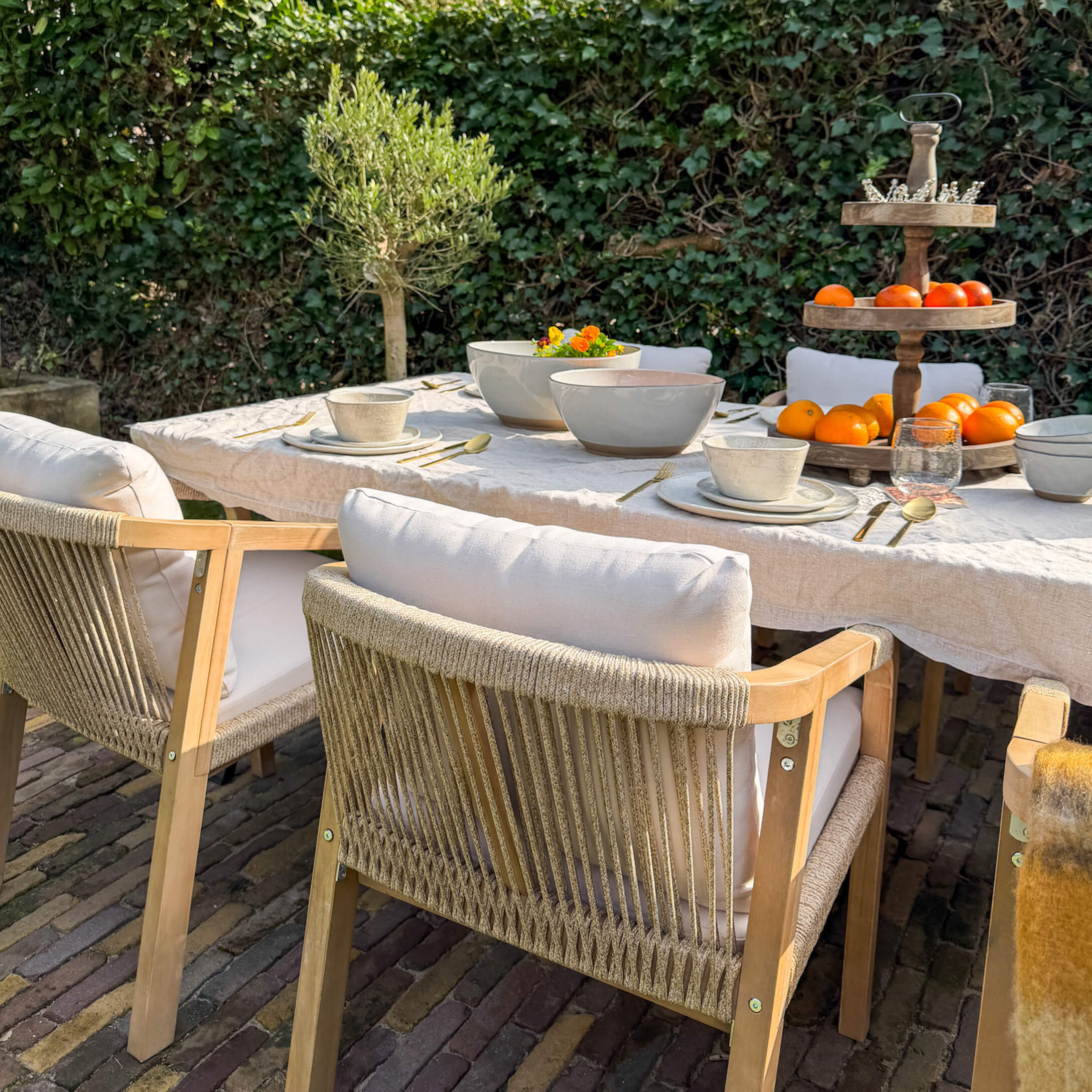 Tuinmeubelset met houten stoelen en witte kussens bij tafel met servies en fruit