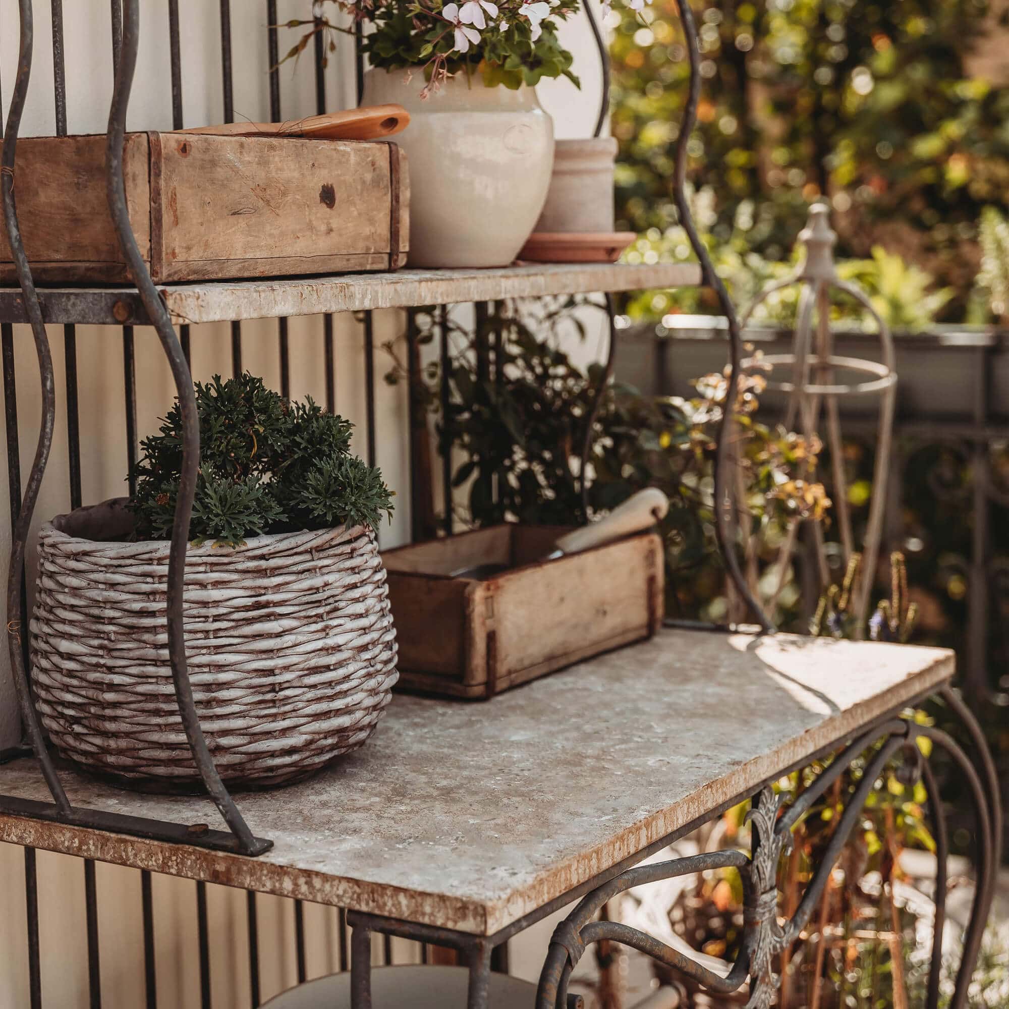 Metalen rek met stenen blad en gevlochten mand met groene plant op het terras