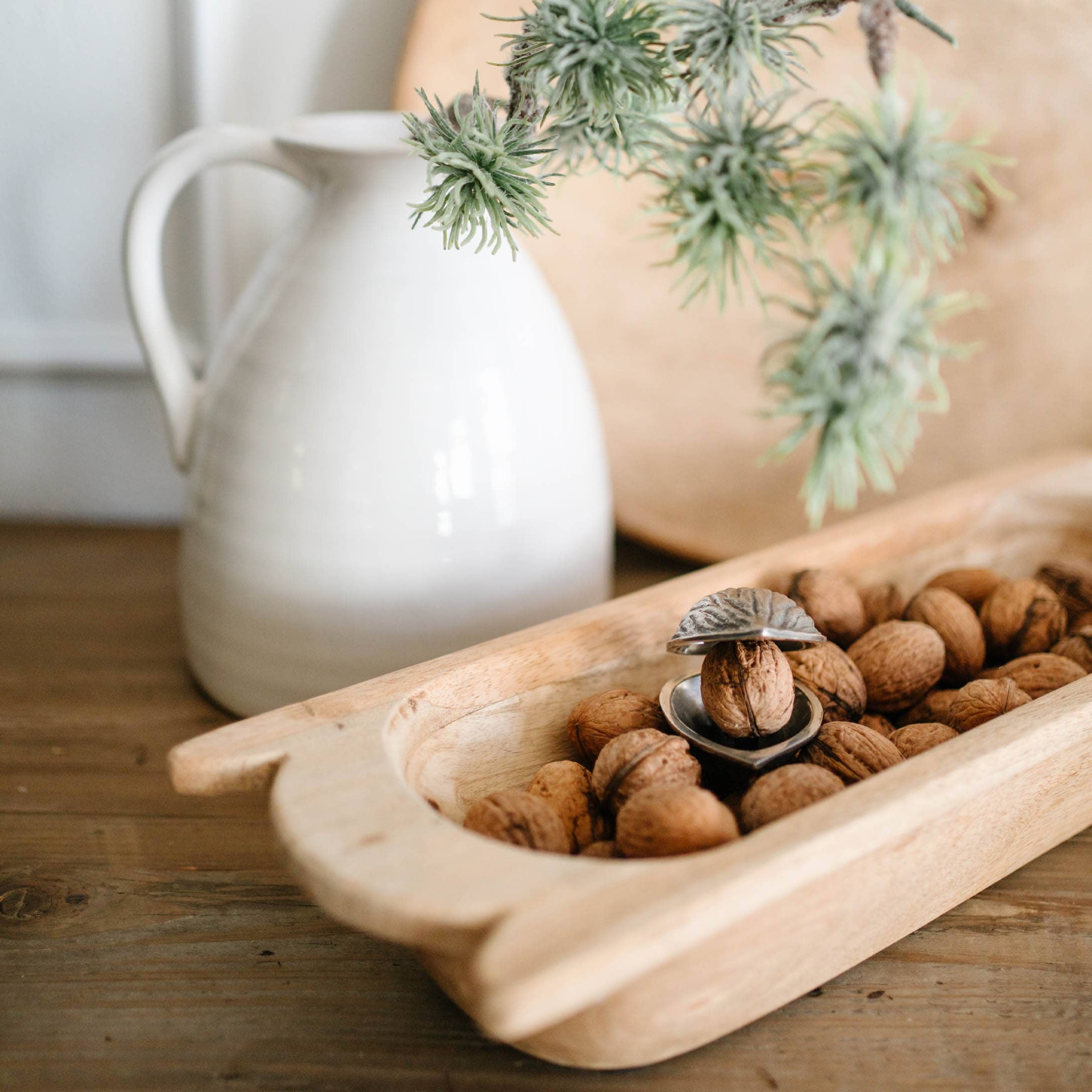 Houten dienblad met walnoten en metalen notenkraker op houten tafel naast witte kan
