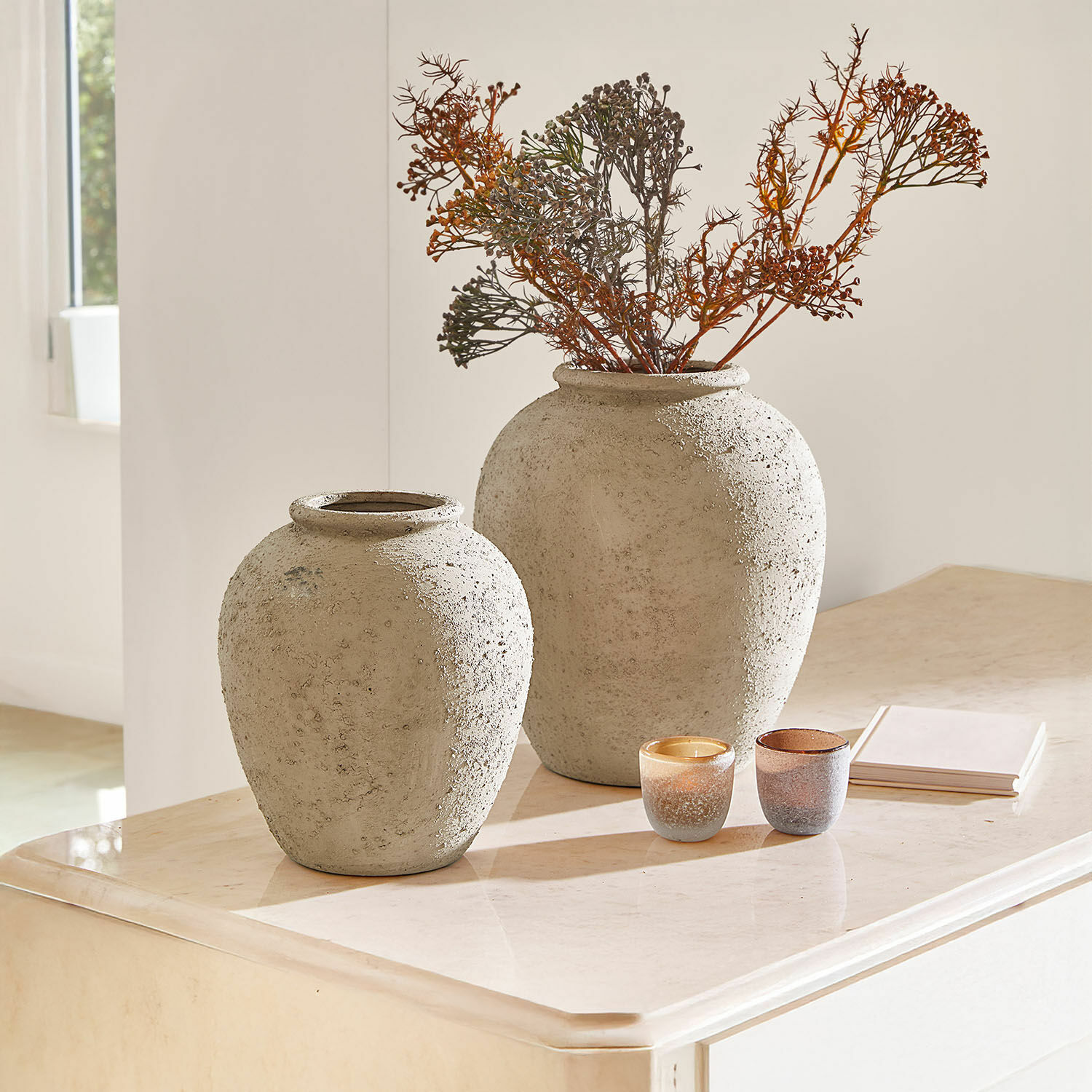 Vaas set van 2 Zaviro Twee grote grijze betonnen vazen op een lichte tafel met droge takken en decoratieve kaarsen
