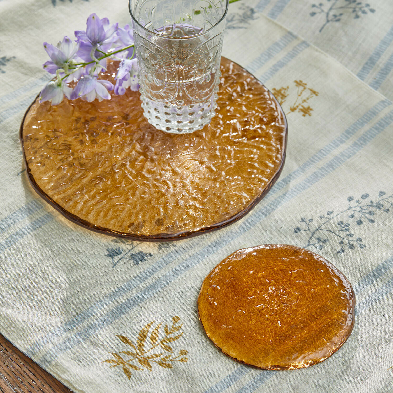 Transparant glazen glas op oranje glazen onderzetter met bloem op linnen tafelkleed