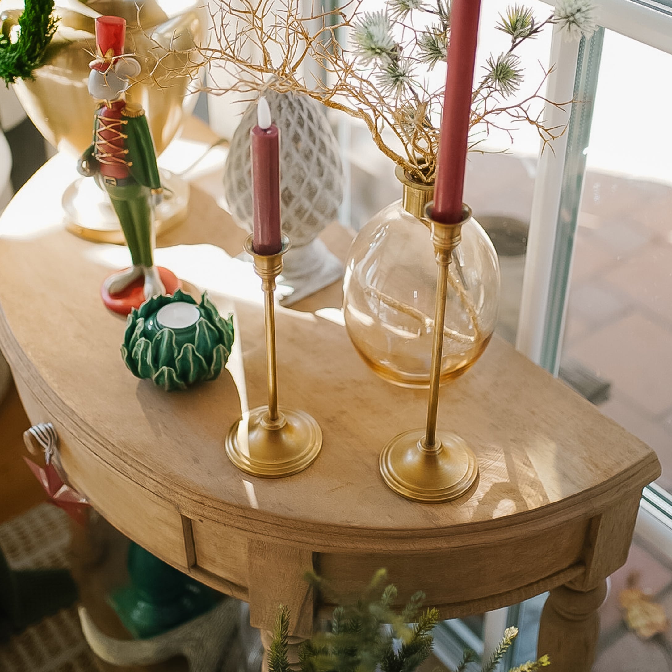 Houten tafel met kerstdecoratie, gouden kandelaars en rode kaarsen bij het raam