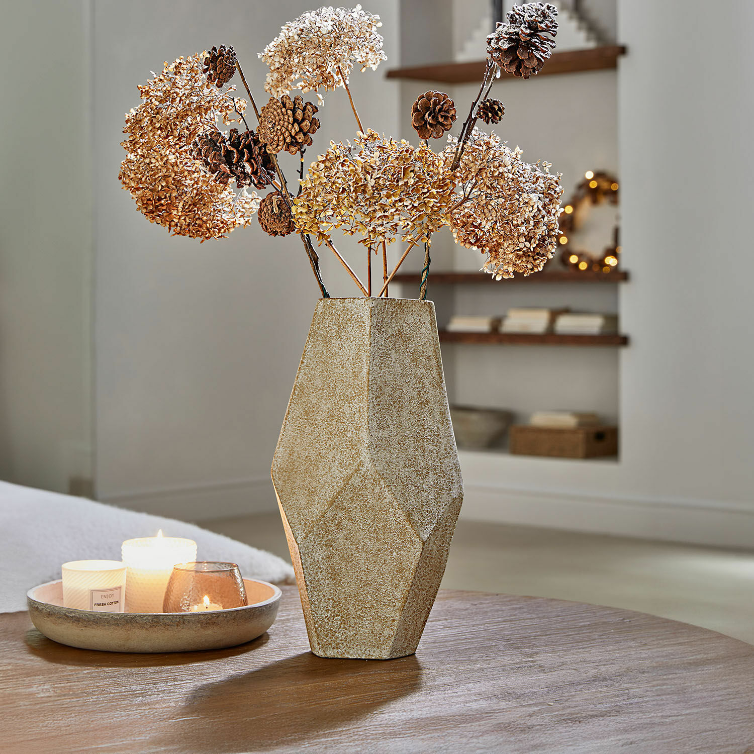 Beige geometrische keramische vaas met gedroogde bloemen en dennenappels op houten tafel