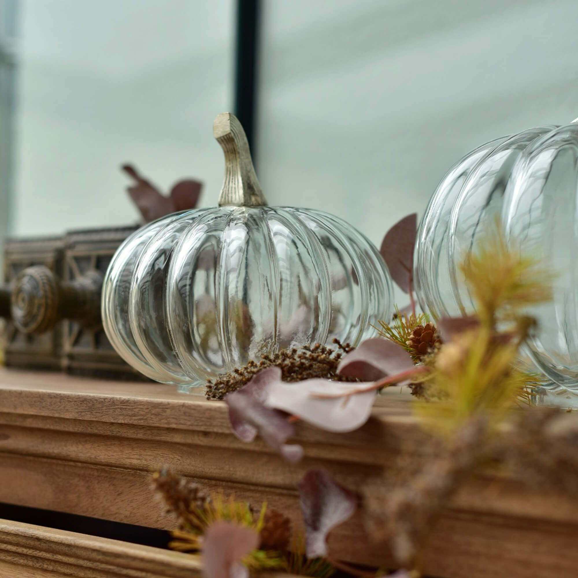 Transparante glazen pompoen met beige steel op houten blad met herfstdecoratie