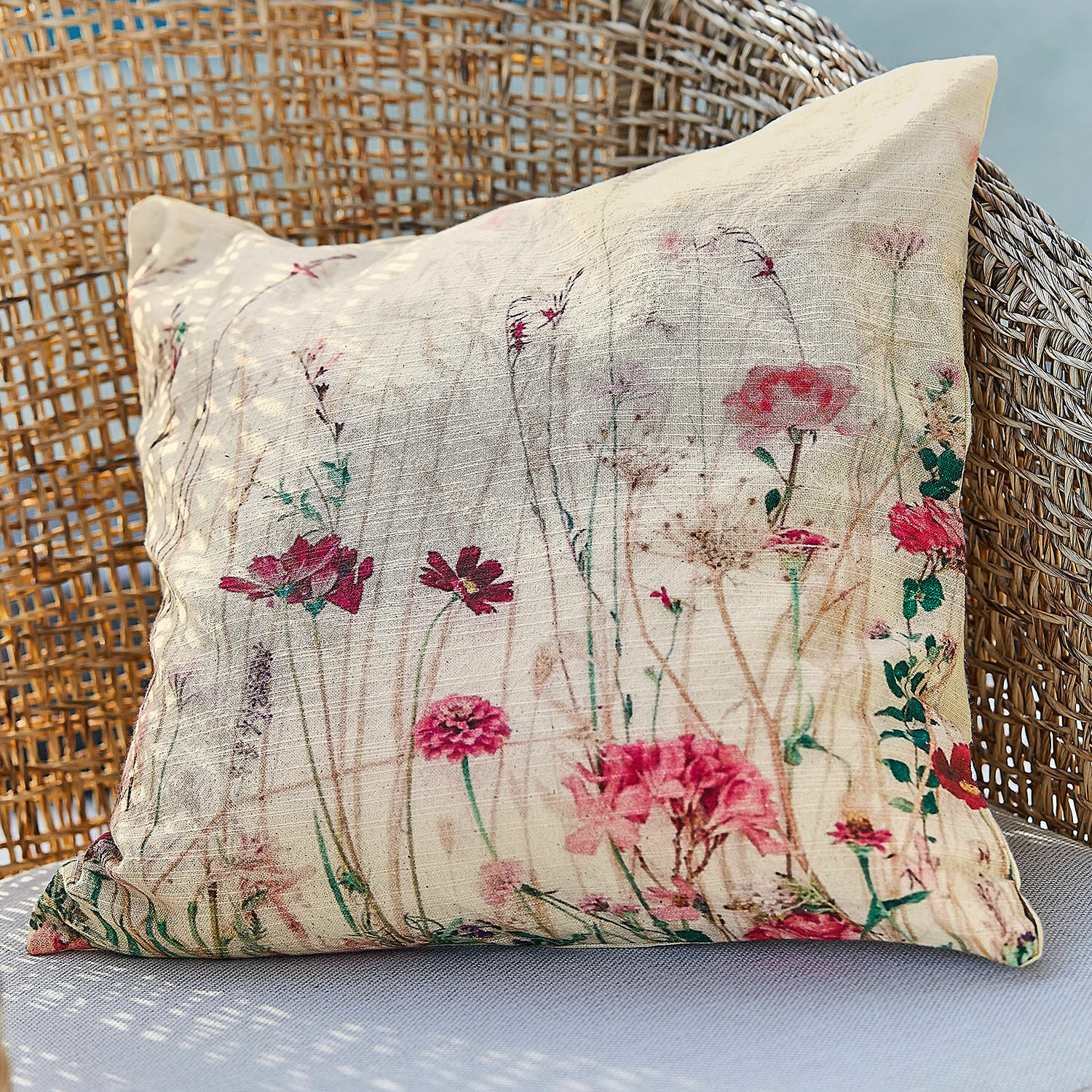 Kussenhoes Briovene Beige kussen van natuurlijke stof met bloemenprint op een rotan stoel, woondecoratie