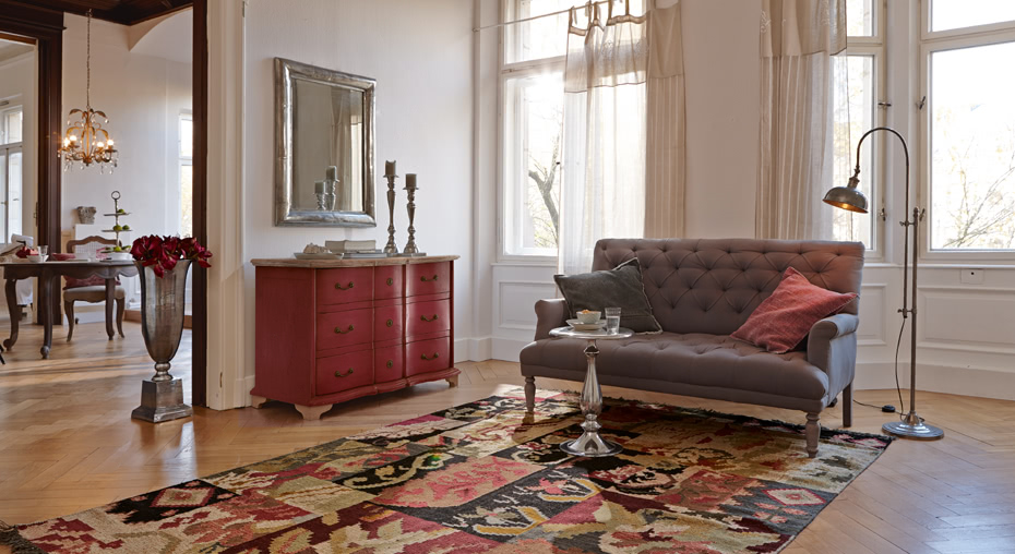 Woonkamer in French chic stijl met grijze gestoffeerde bank, rode houten kast en kleurrijk vloerkleed