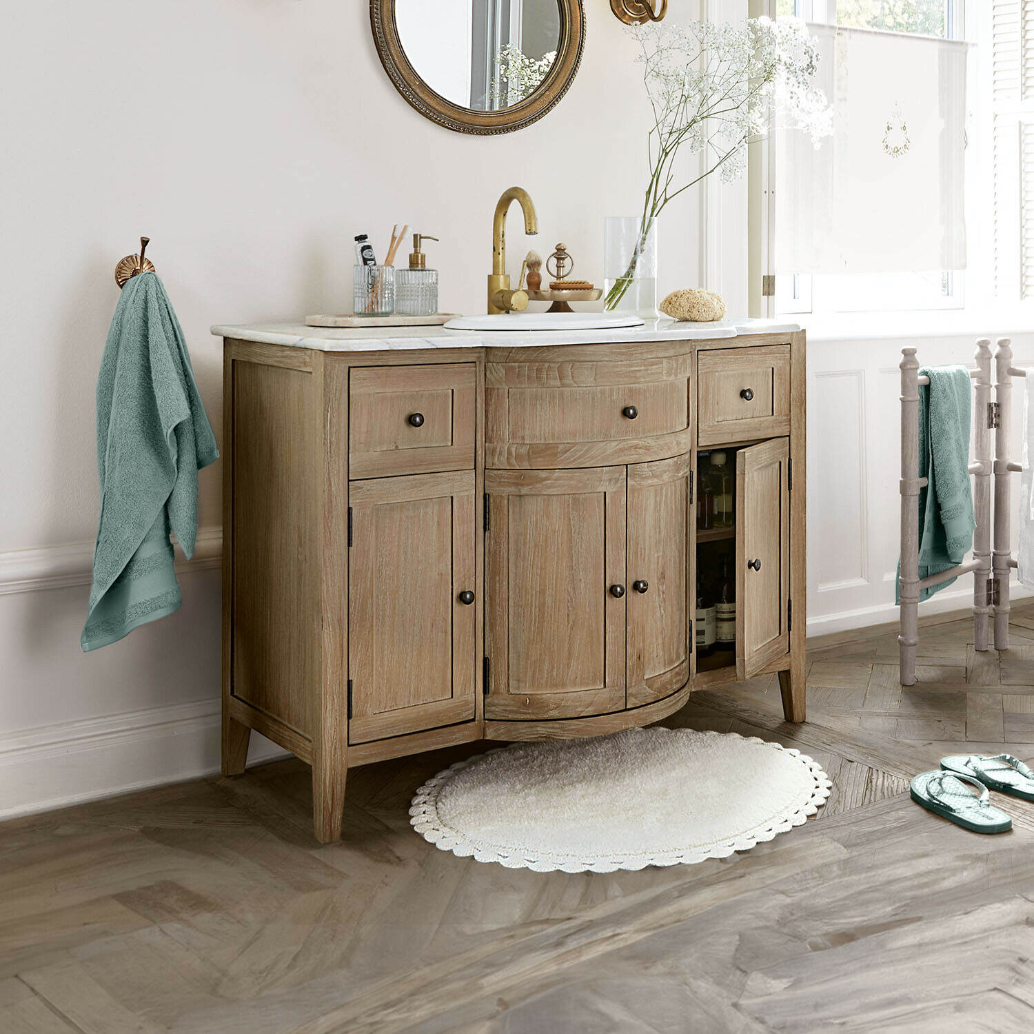Houten badkamerkast met marmeren blad, gouden kraan, muntgroene handdoeken en ronde mat