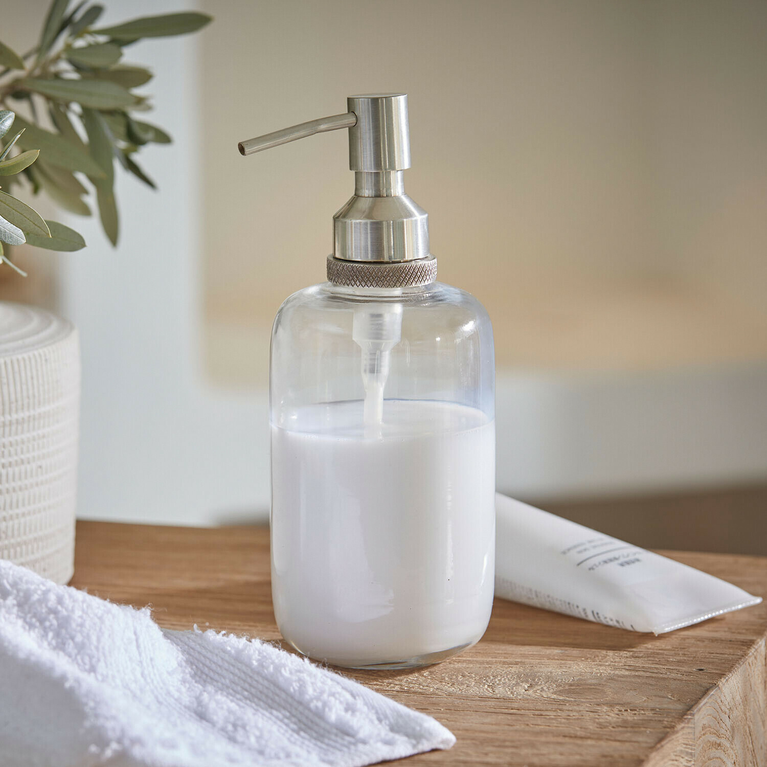 Transparante zeepdispenser van roestvrij staal met witte vloeistof op houten oppervlak