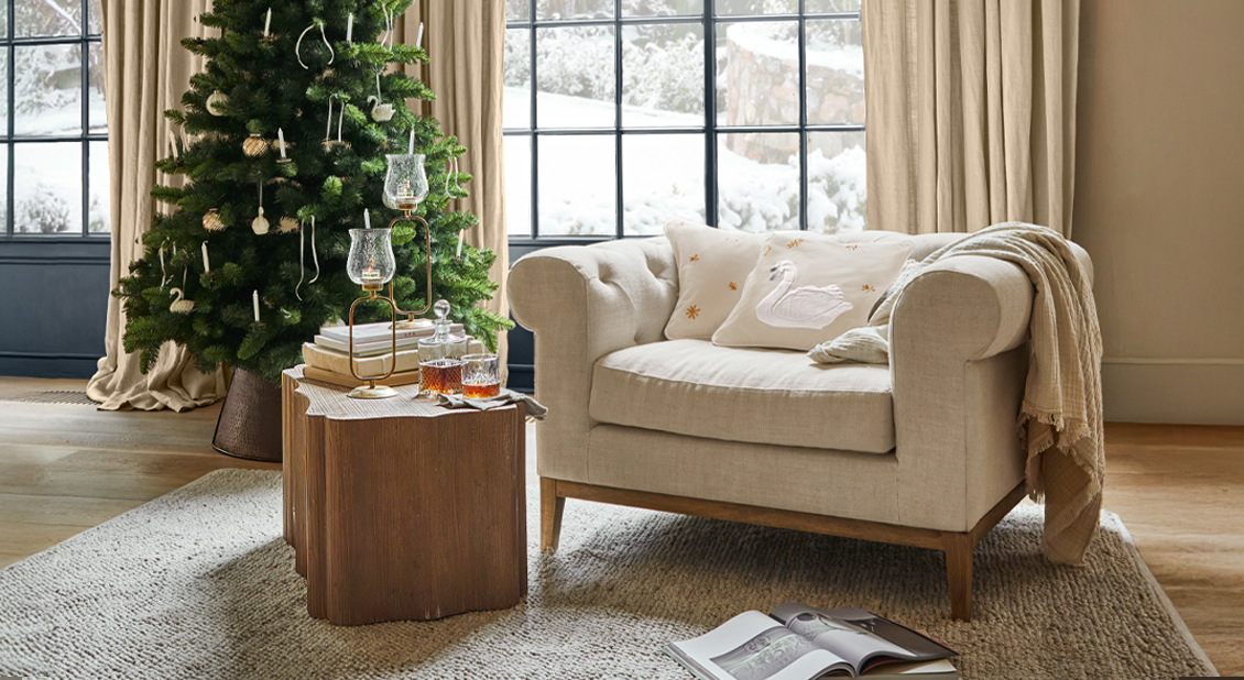 Beige bank met sierkussen met zwaanmotief naast versierde kerstboom in gezellige winterse woonkamer