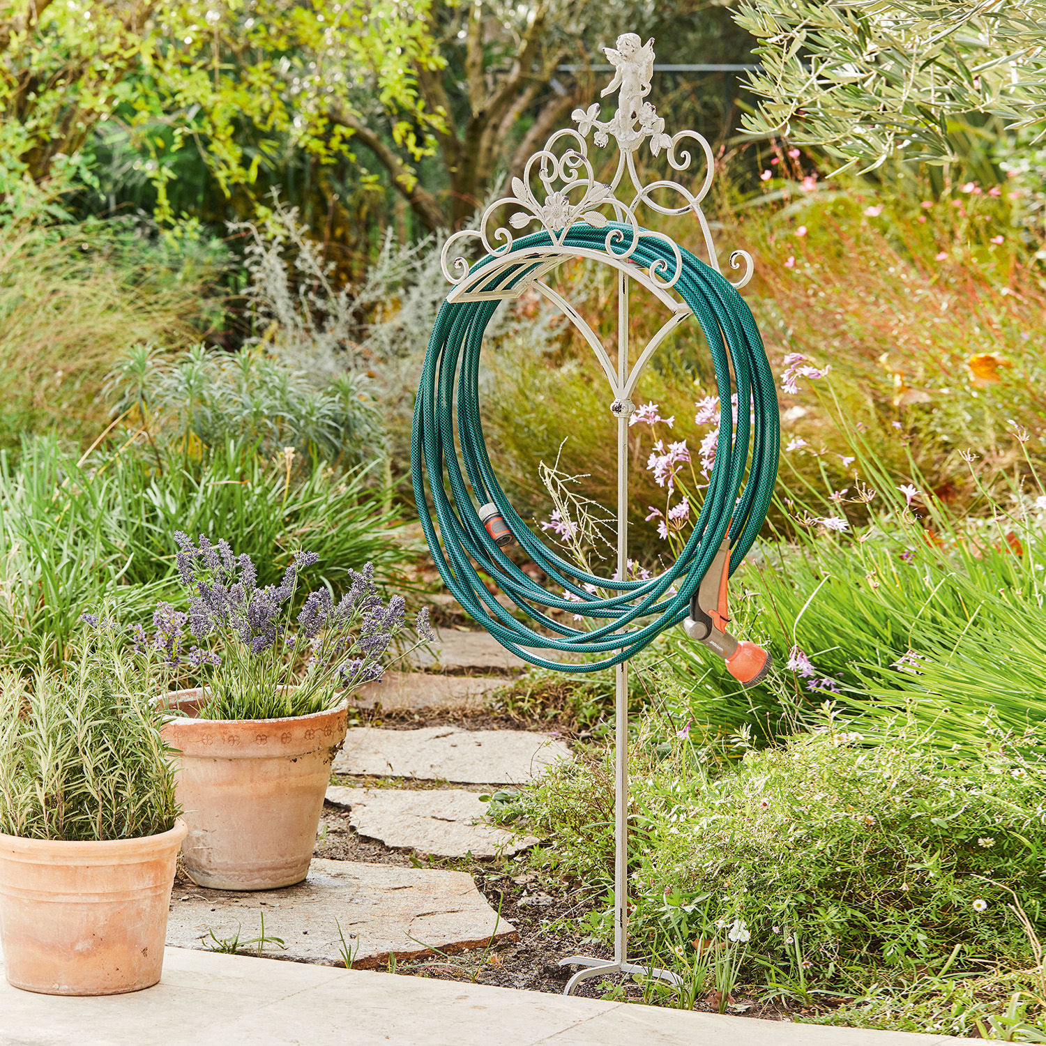 Witte metalen tuinslanghouder in vintage stijl in groene tuin met tuinslang
