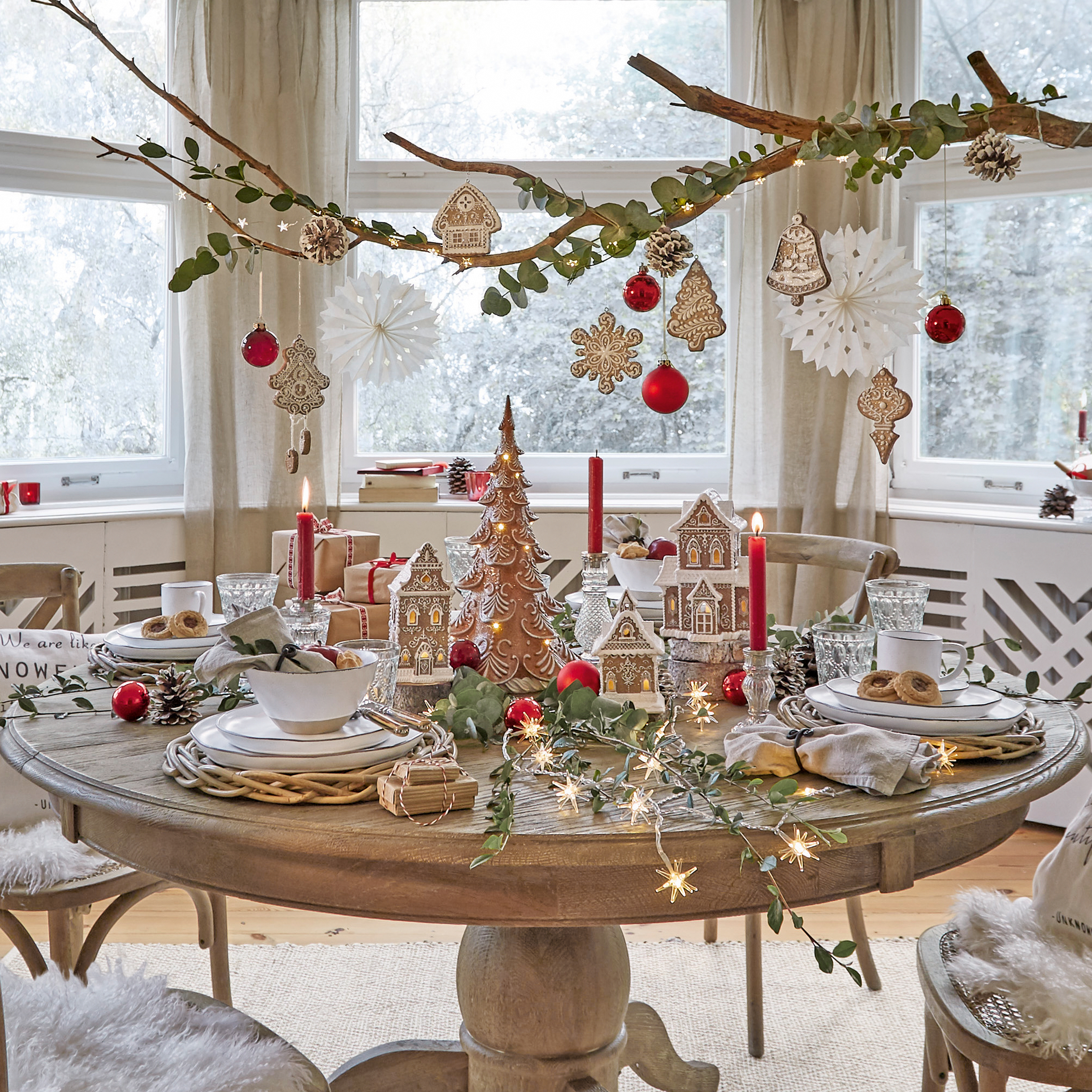 Houten ronde tafel met kerstdecoratie van peperkoekhuisjes, rode ballen en brandende kaarsen
