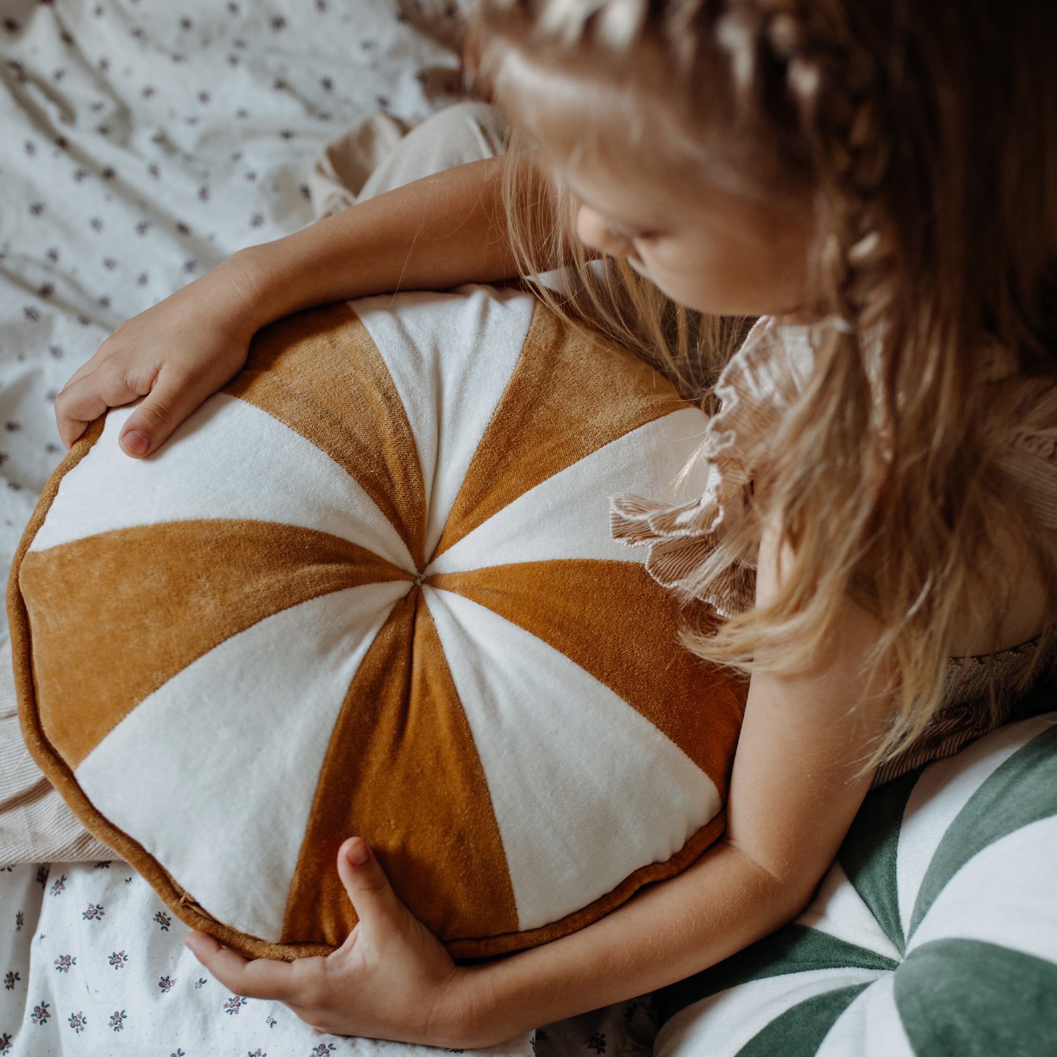 Meisje houdt ronde fluwelen kussen vast in wit en bruin, gezellige kinderkamerdecoratie