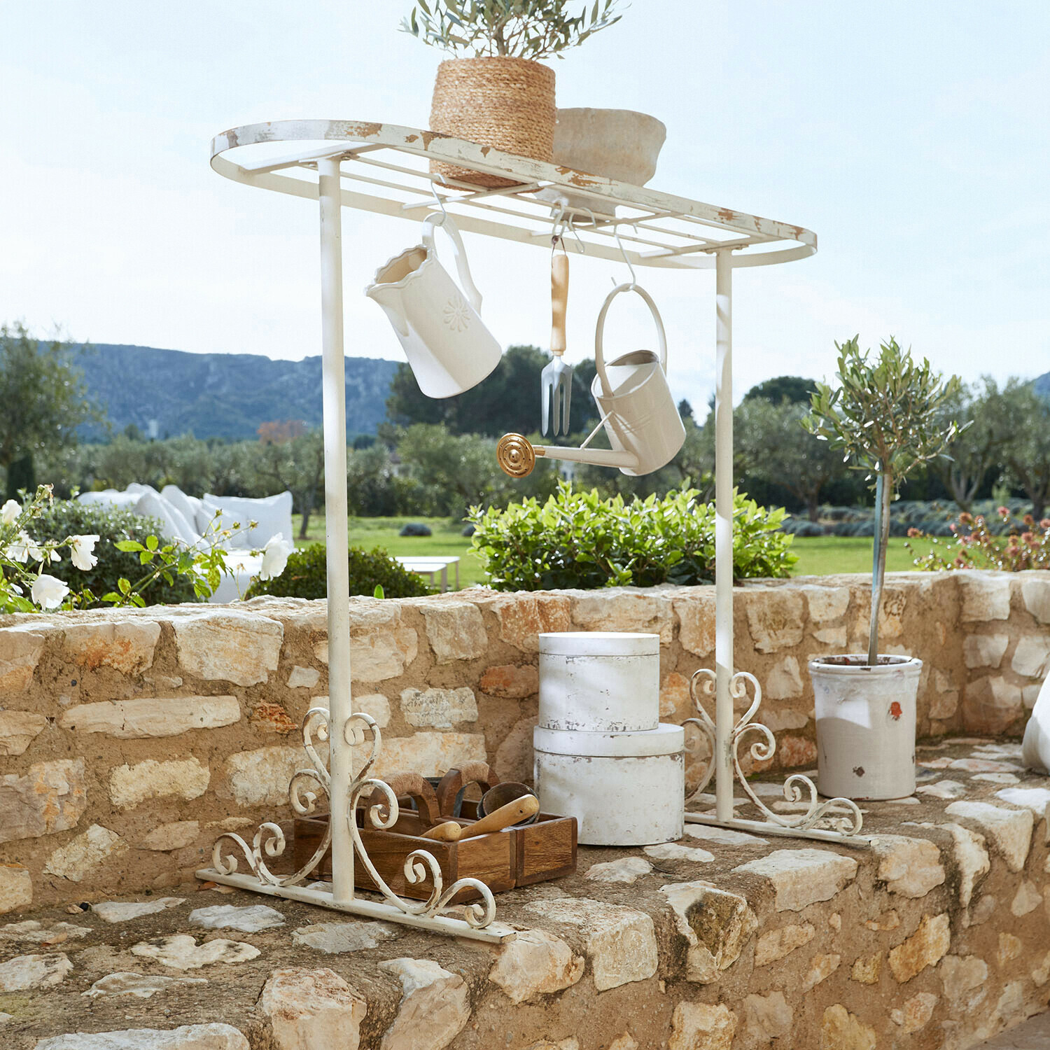 Onderstel voor plantentafel Mairoux Witte metalen tuinplank met hangende accessoires en bloempot op stenen muur in tuin
