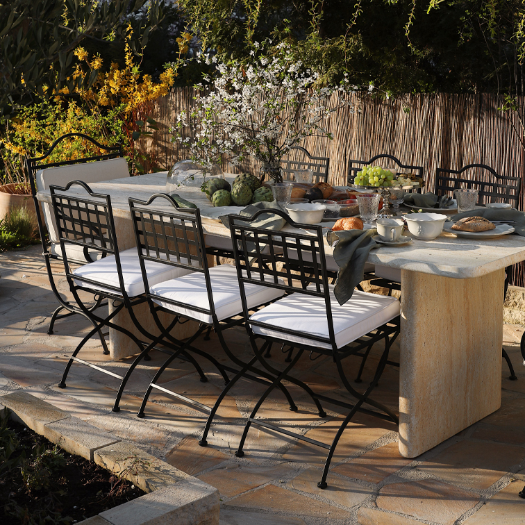 Tuin tafel van steen met zwarte metalen stoelen en witte kussens, buiten gedekte tafel met decoratie