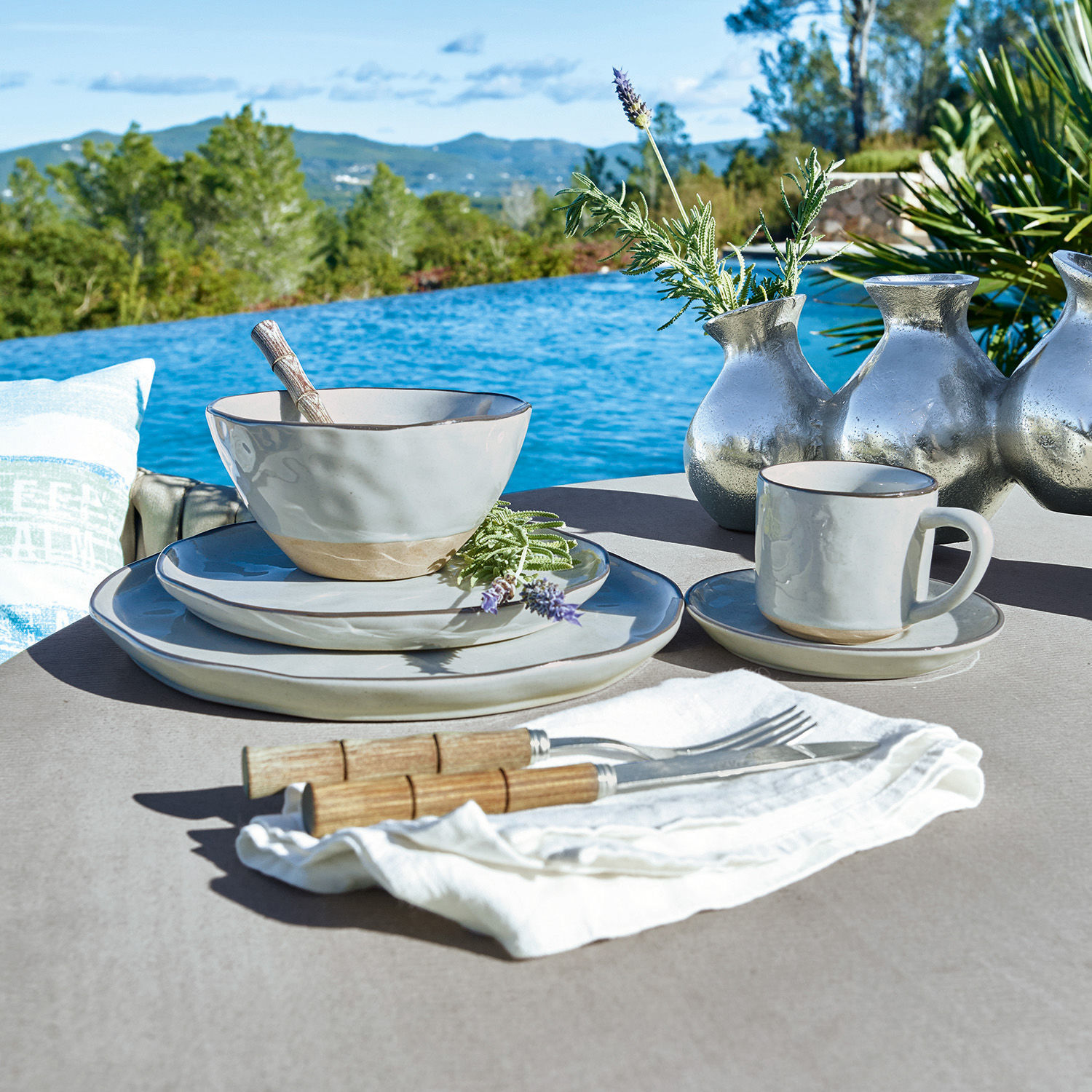 Beige keramiek servies met houten bestek op tafel bij zwembad met bergzicht
