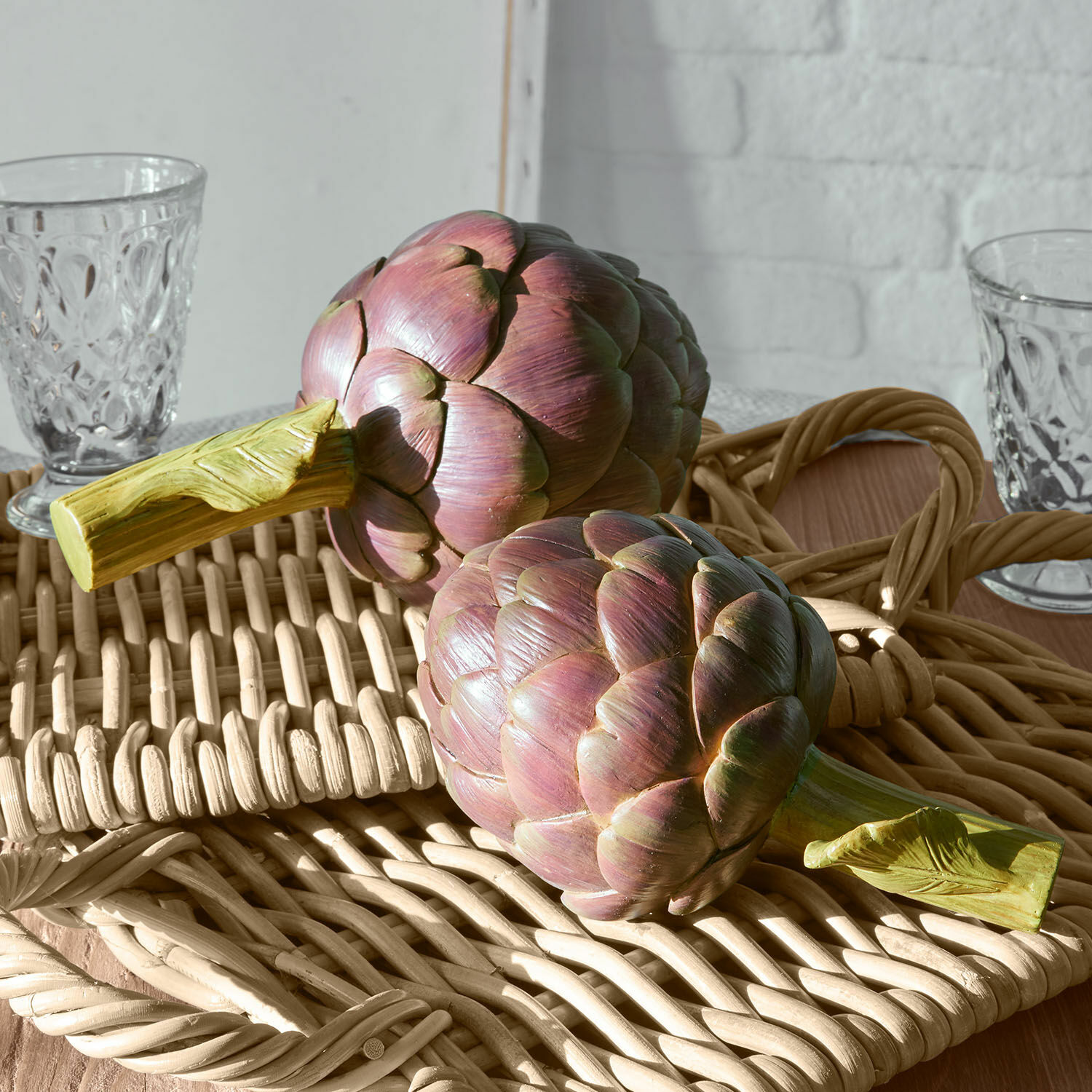 Decoratieve artisjokken van kunststof in paarsgroene kleur op een rieten dienblad voor interieurdecoratie