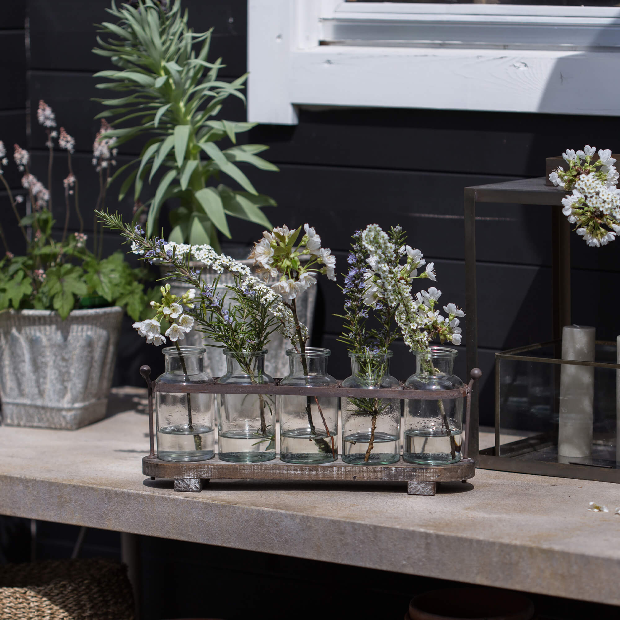 Glazen flesjes met witte bloemen in metalen houder op stenen tafel, tuindecoratie