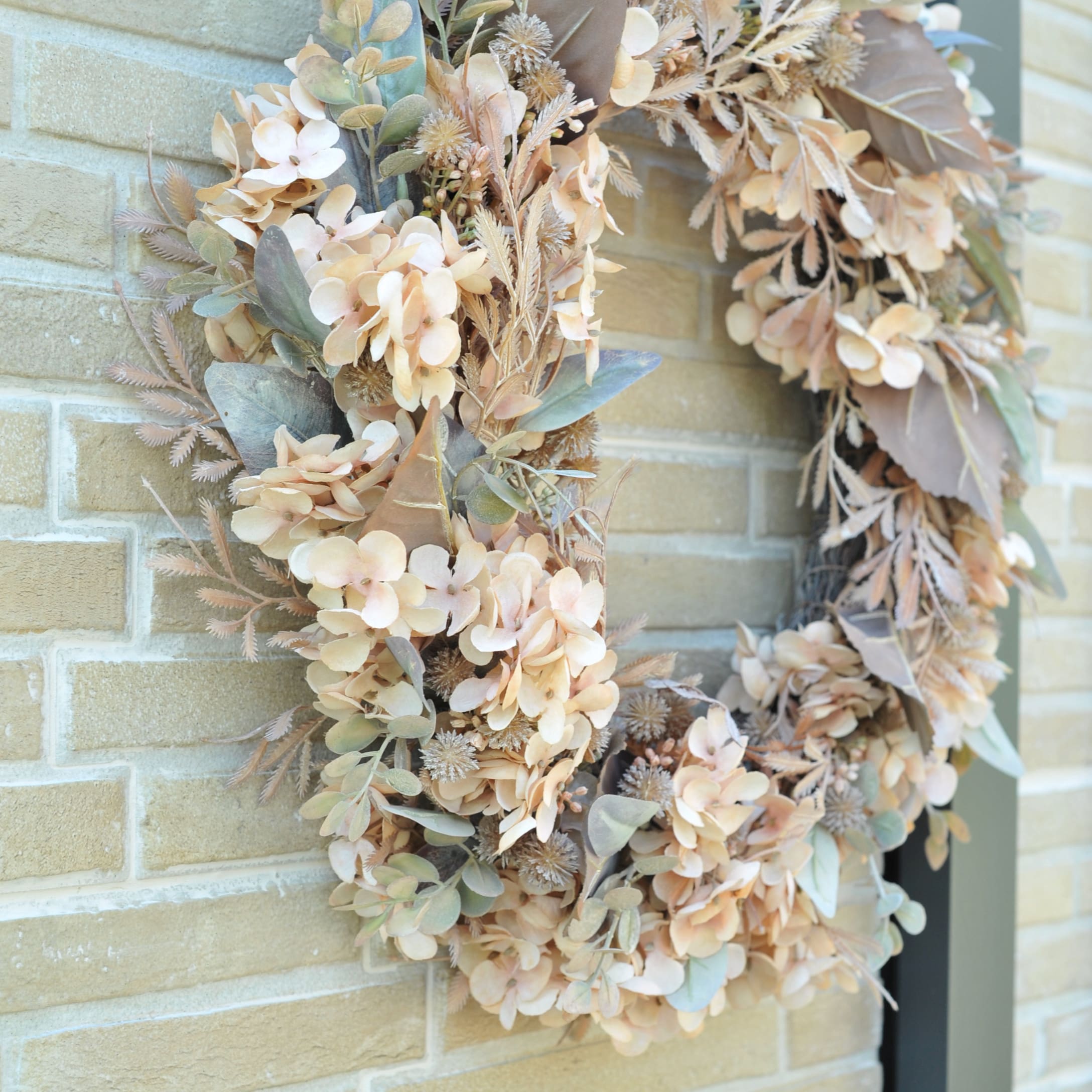 Herfstdecoratieve krans van beige en groene kunstbloemen aan bakstenen muur
