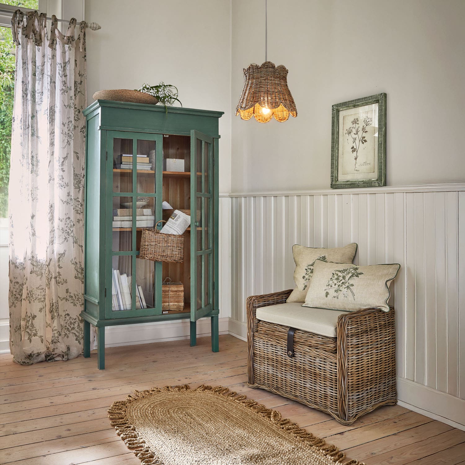 Groene houten vitrinekast en rotan bank met kussens in lichte kamer met natuurlijke vloerkleed