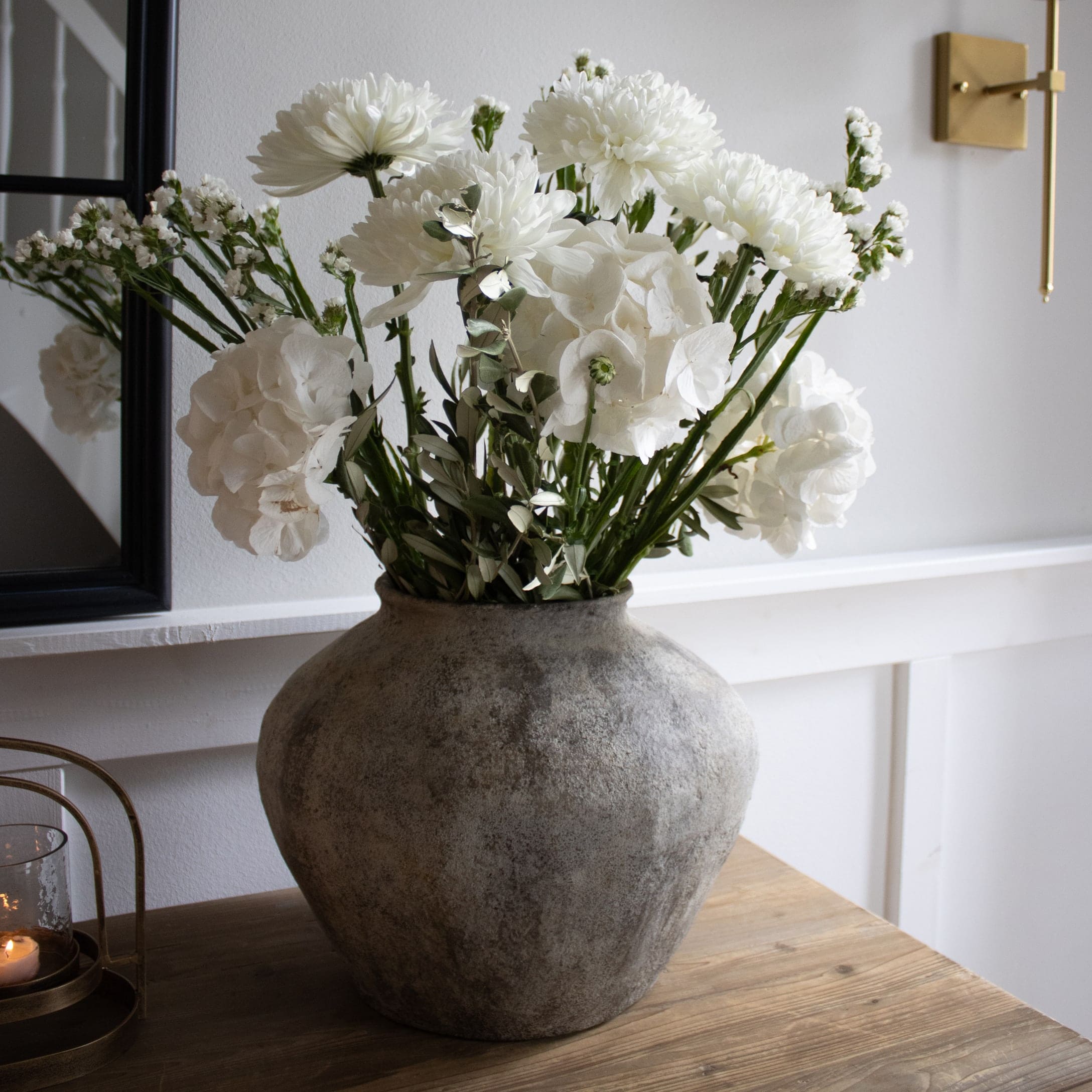 Grote grijze keramische vaas met witte bloemen op houten tafel in lichte kamer