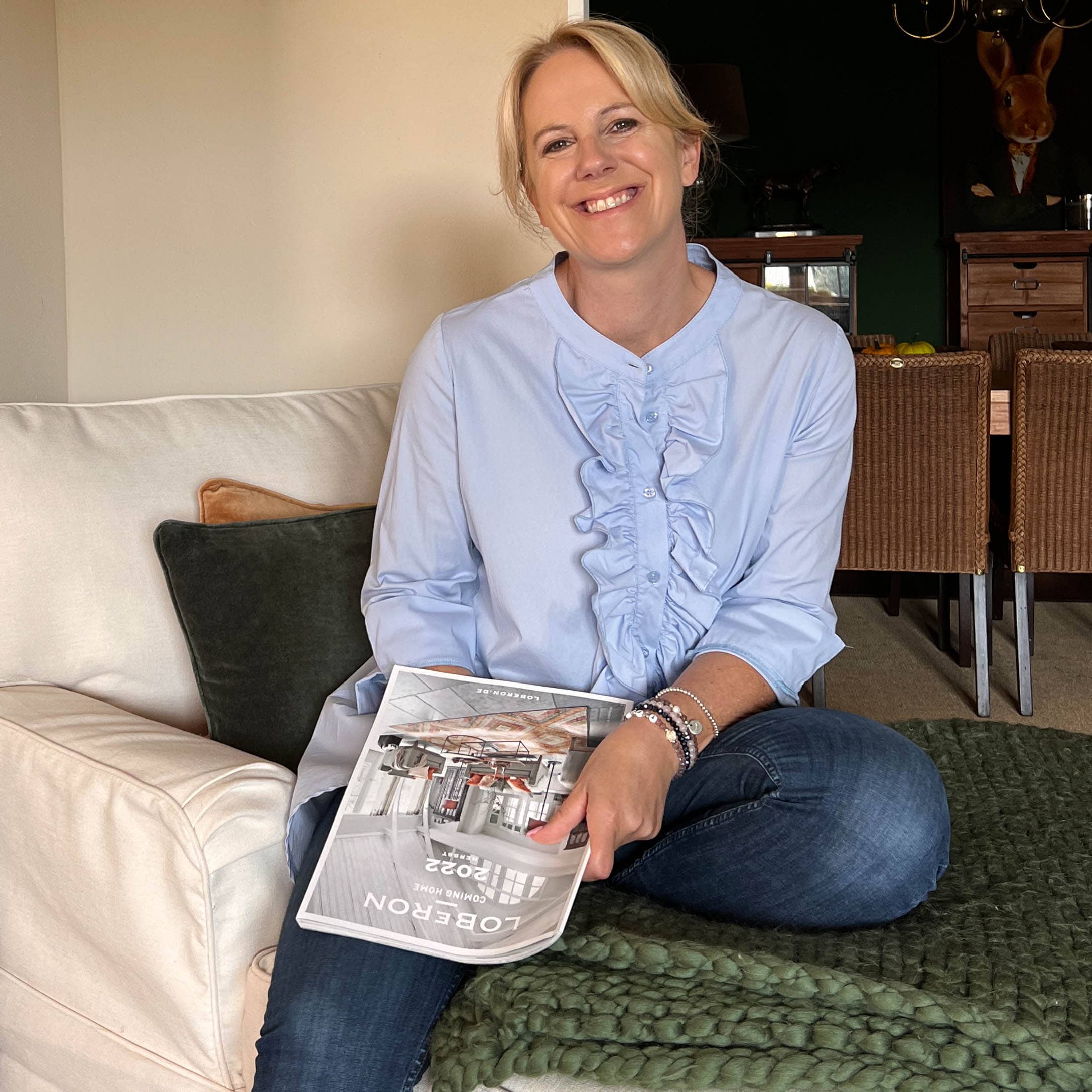Vrouw zittend op bank met Loberon tijdschrift, gezellige woning met gebreide deken en kussens