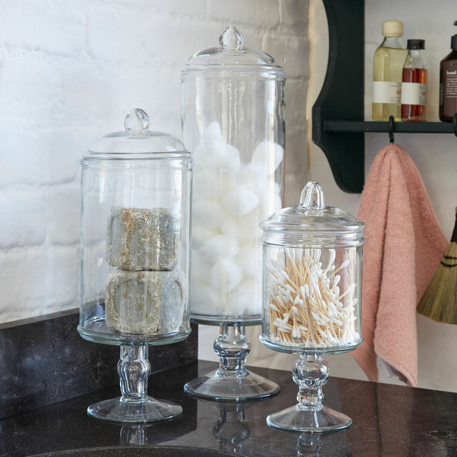 Drie transparante glazen potten op voet met deksels voor badkameropslag