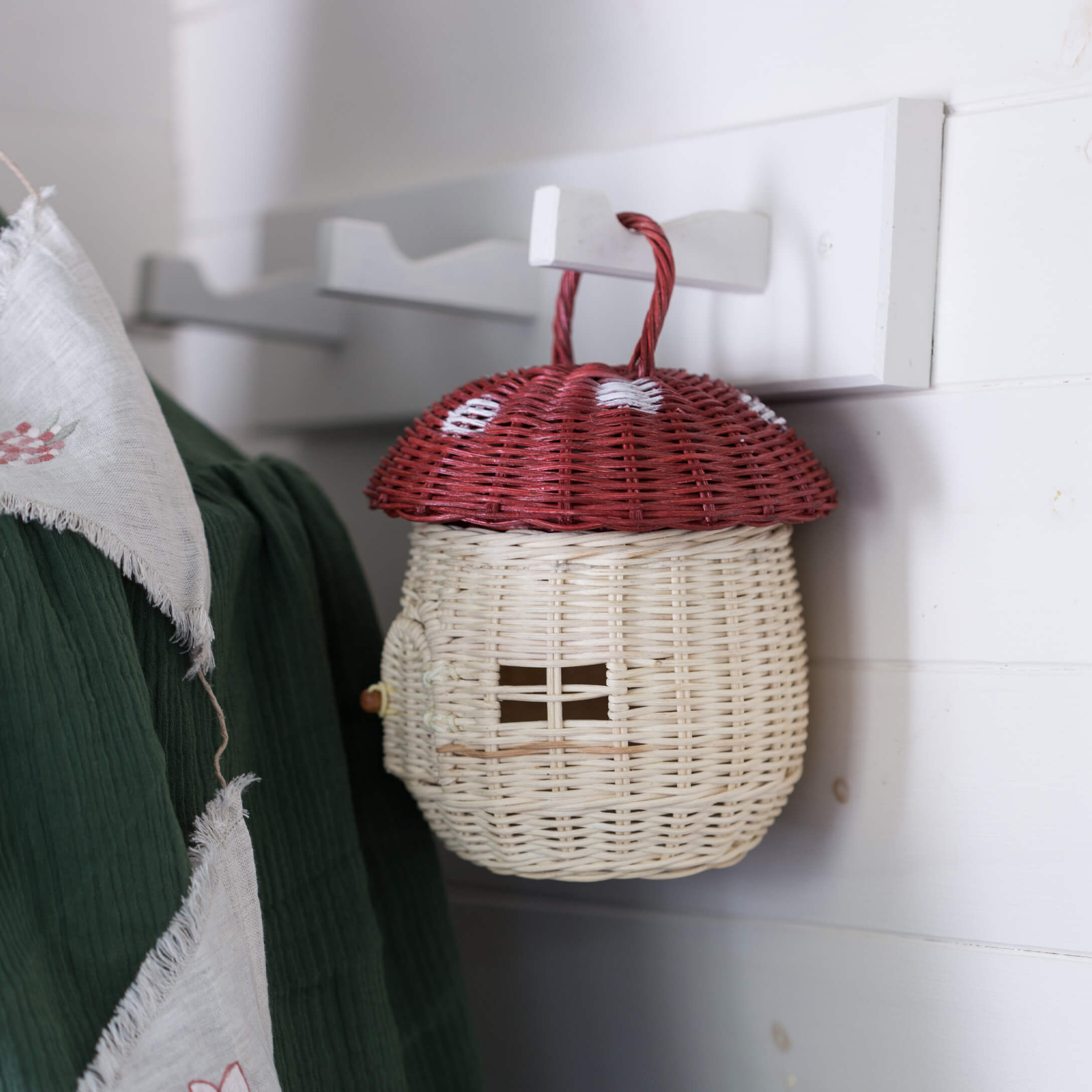 Decoratieve rieten mand in de vorm van een rode paddenstoel met rode hoed en witte steel, hangend aan een haak