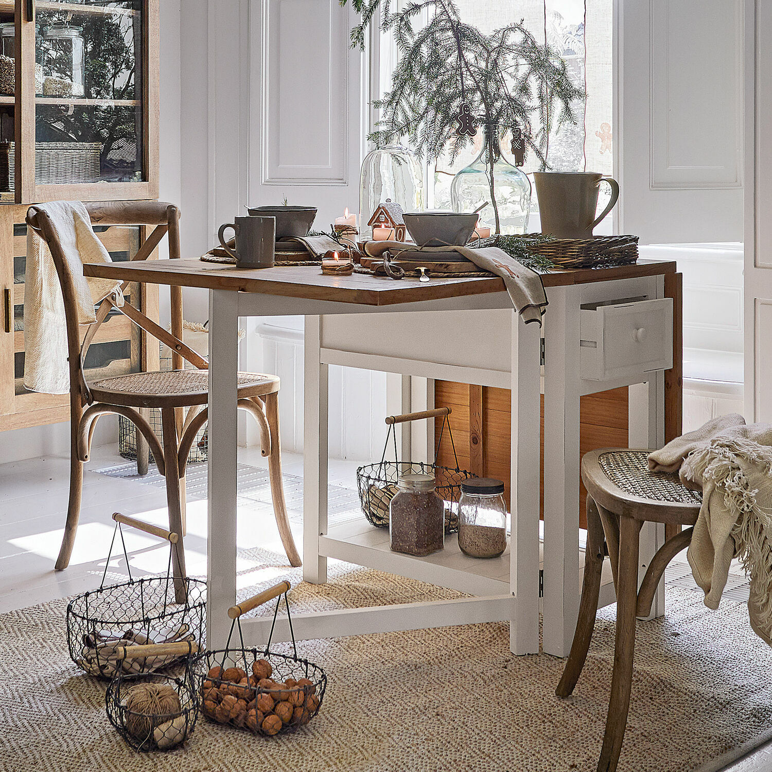 Eetkamer met witte houten tafel en natuurlijke rieten stoelen, kerstdecoratie en manden met noten
