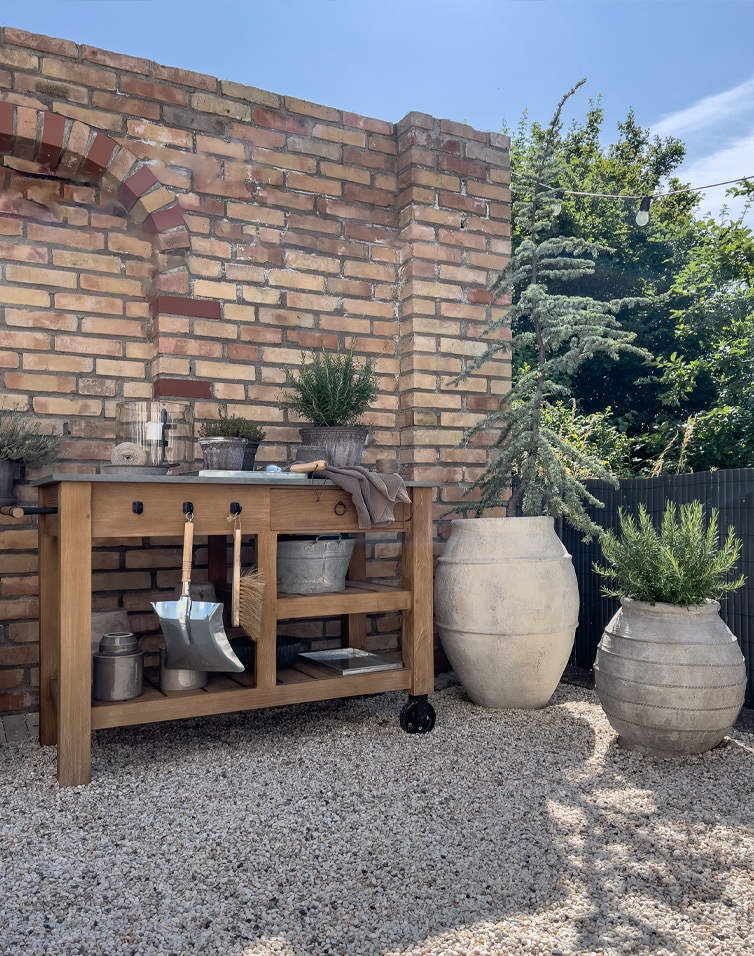 Houten tuintafel met metalen blad en tuingereedschap aan bakstenen muur op grindvloer