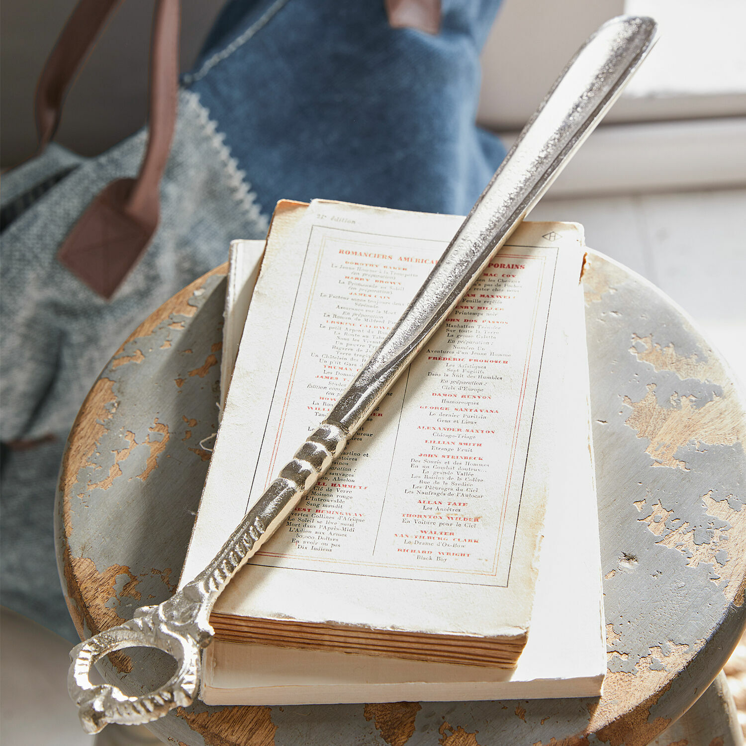 Schoenlepel Lucas Zilverkleurige metalen flesopener op oude tafel met boeken en tas op de achtergrond