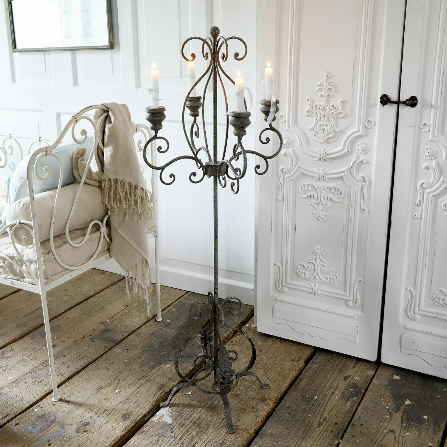 Staande smeedijzeren kandelaar in vintage stijl met vijf witte kaarsen op een houten vloer