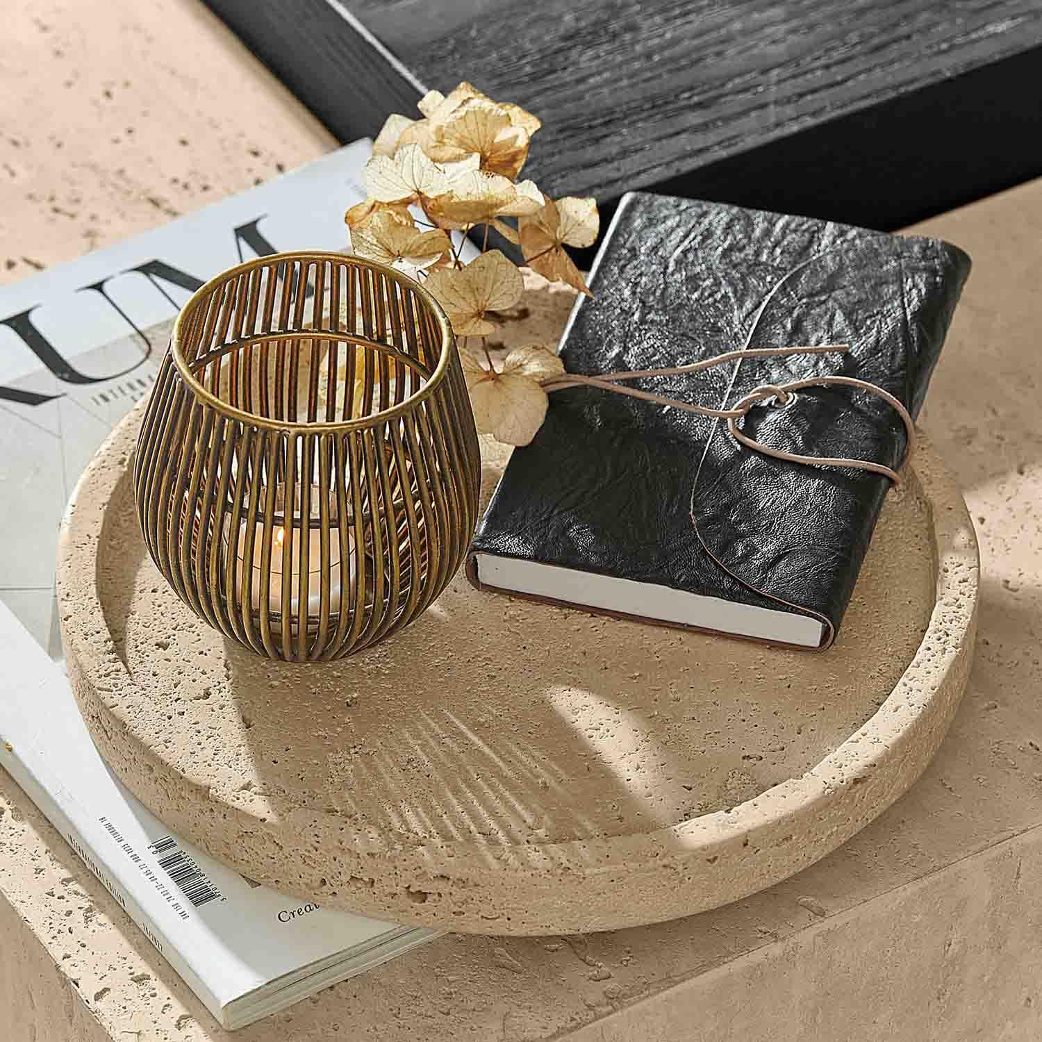 Ronde stenen tray met zwart leren notitieboek en gouden kaarsenhouder op tafel