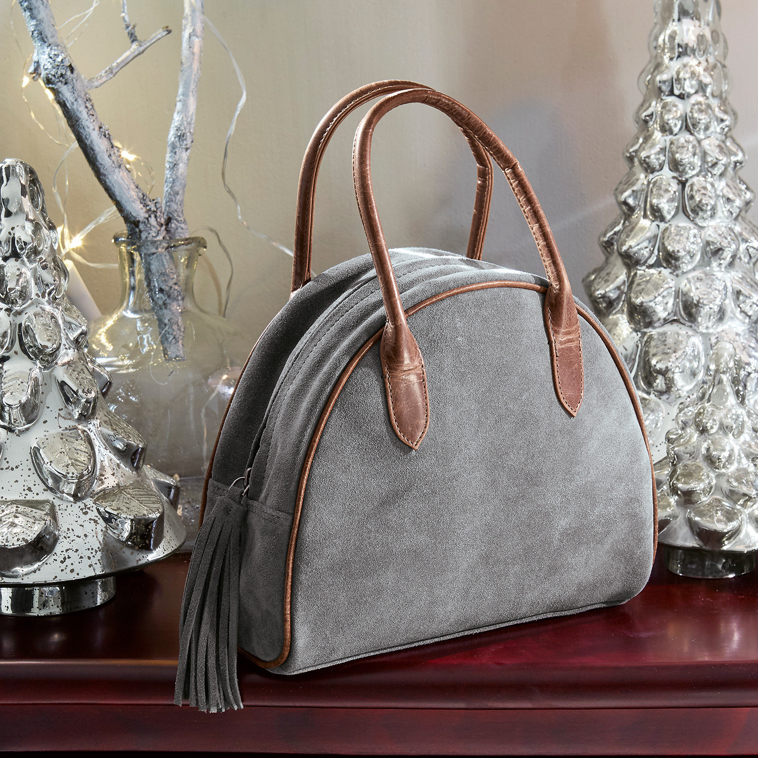 Tas Elisabeta Grijze suède tas met bruine leren handvatten en franjes op tafel met kerstdecoratie