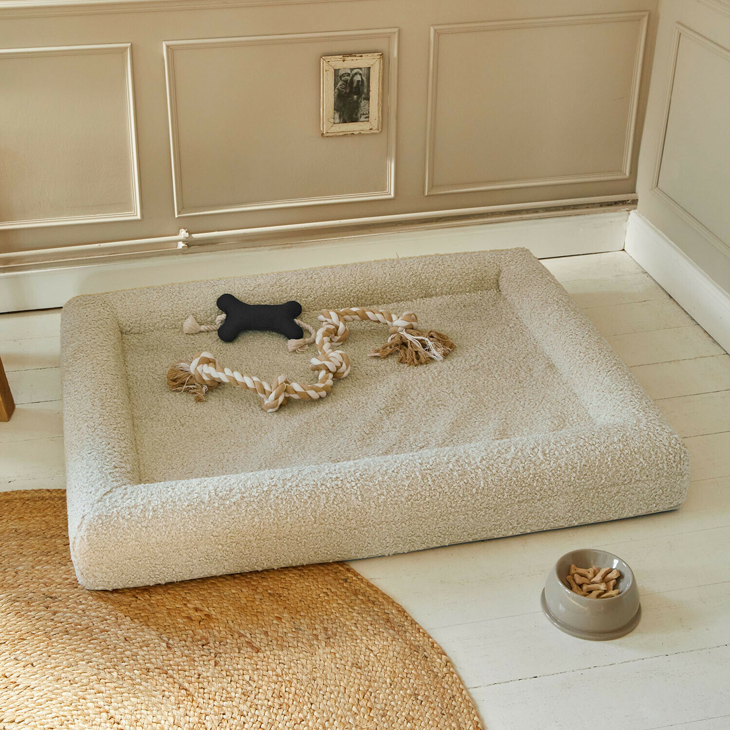 Beige hondenmand van zacht materiaal met speelgoed en voerbak met snacks op lichte vloer