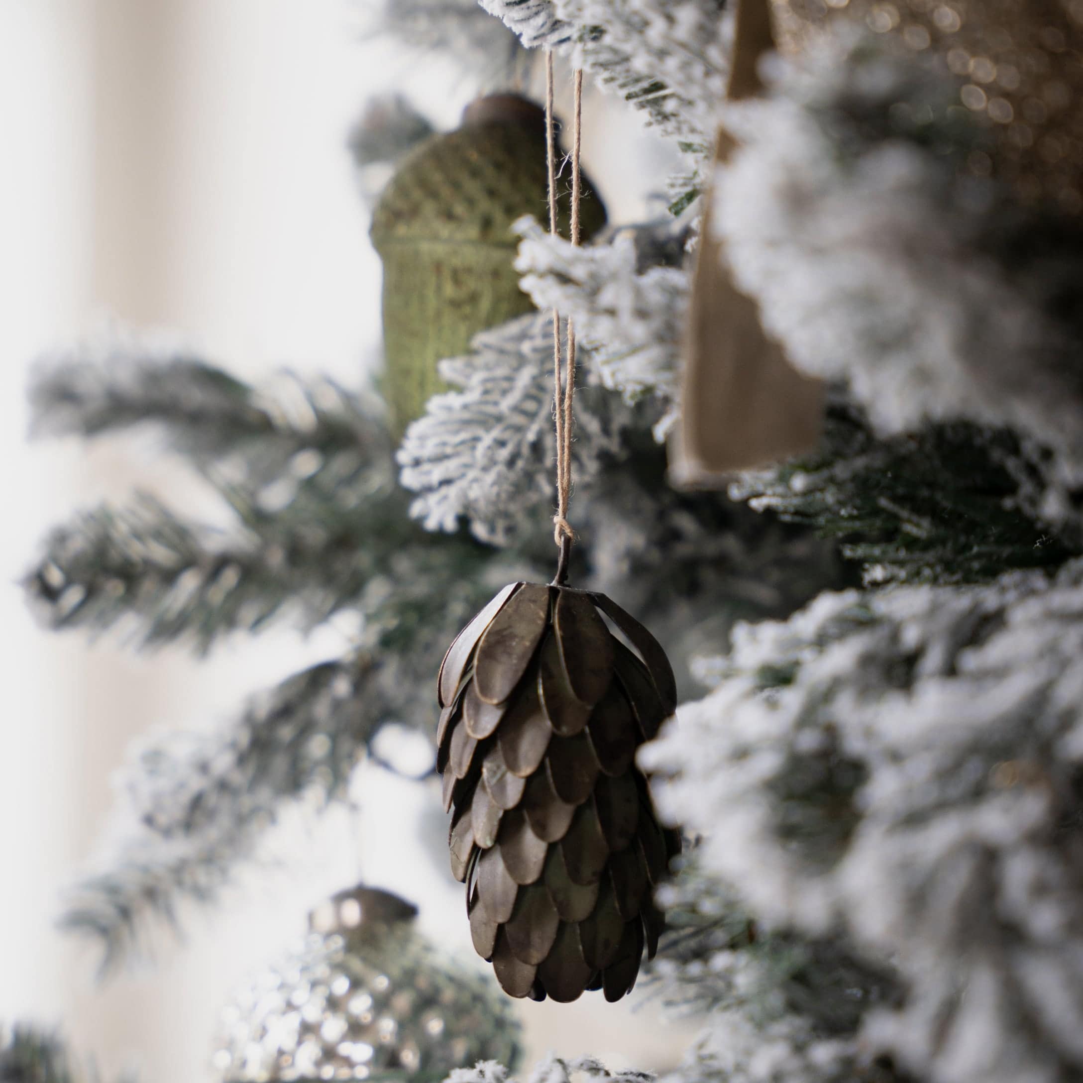 Metalen dennenappel kerstversiering in bruine kleur aan besneeuwde kerstboom