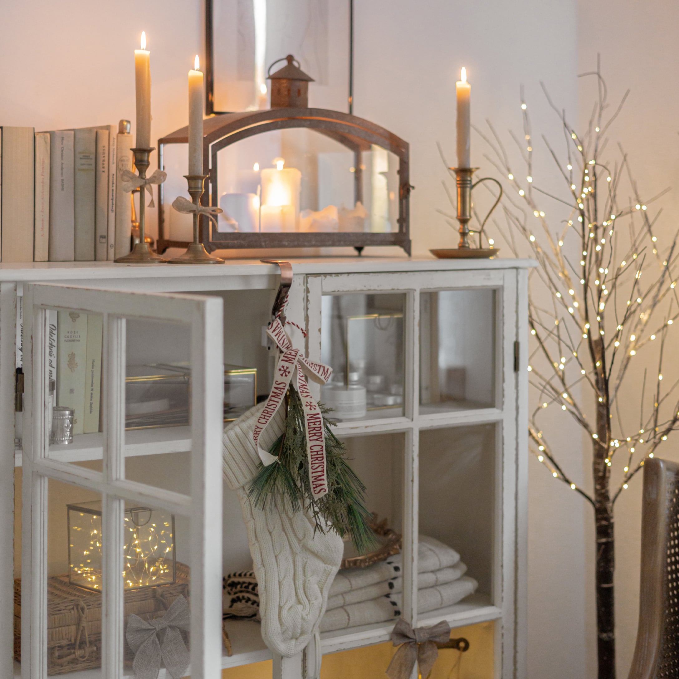 Witte gebreide kerstkous met groene takken aan witte houten kast met kaarsdecoratie