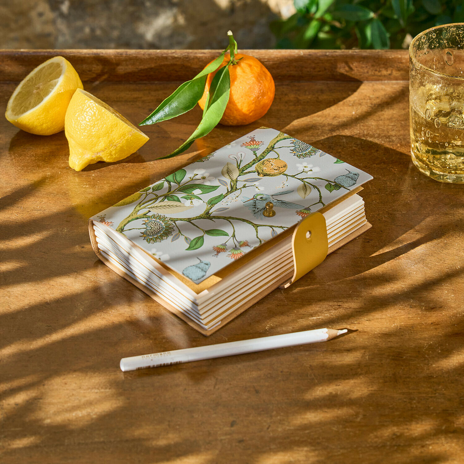 Notitieboekje Ambroisea Notitieboek met decoratieve plantenprint en gele sluiting op houten tafel met citroen en mandarijn