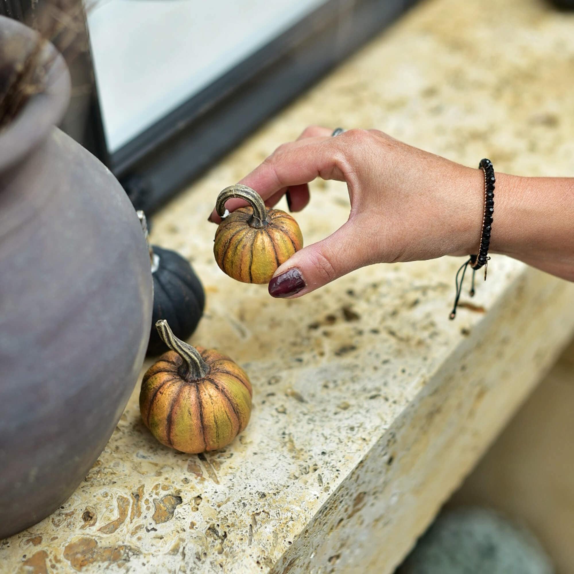 Hand houdt kleine decoratieve oranje-bruin pompoen vast op een stenen oppervlak