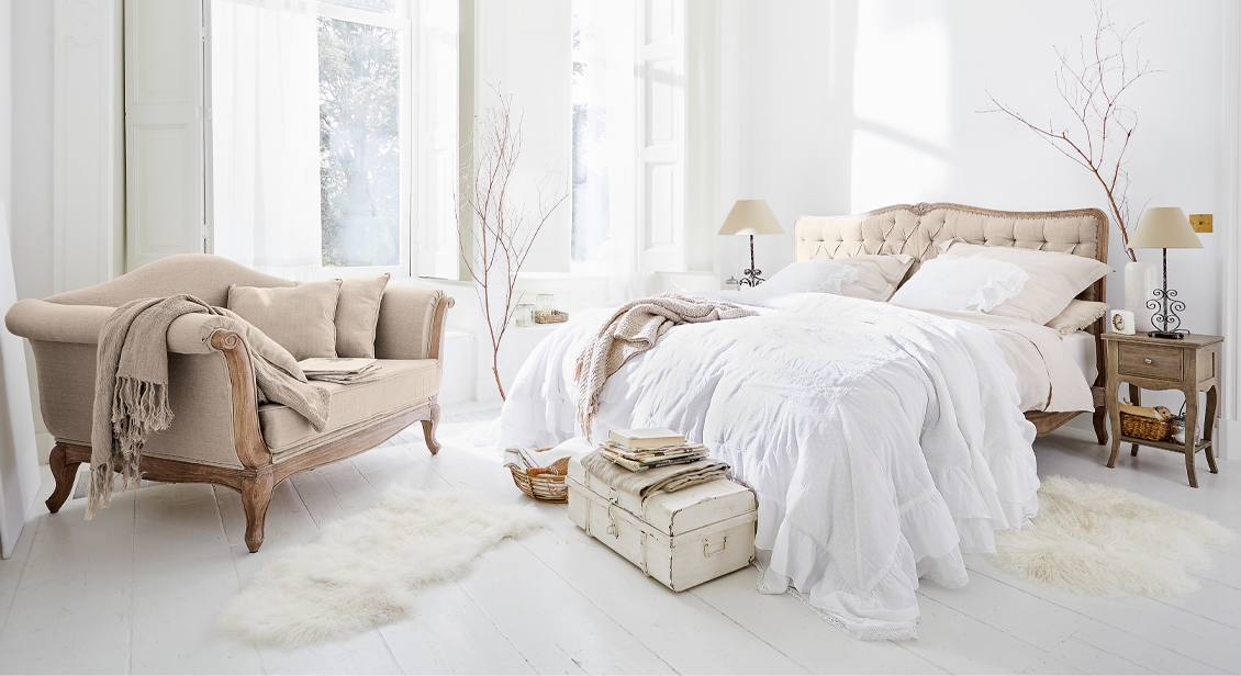 Gezellige slaapkamer met beige gestoffeerd bed en vintage bank op lichte houten vloer