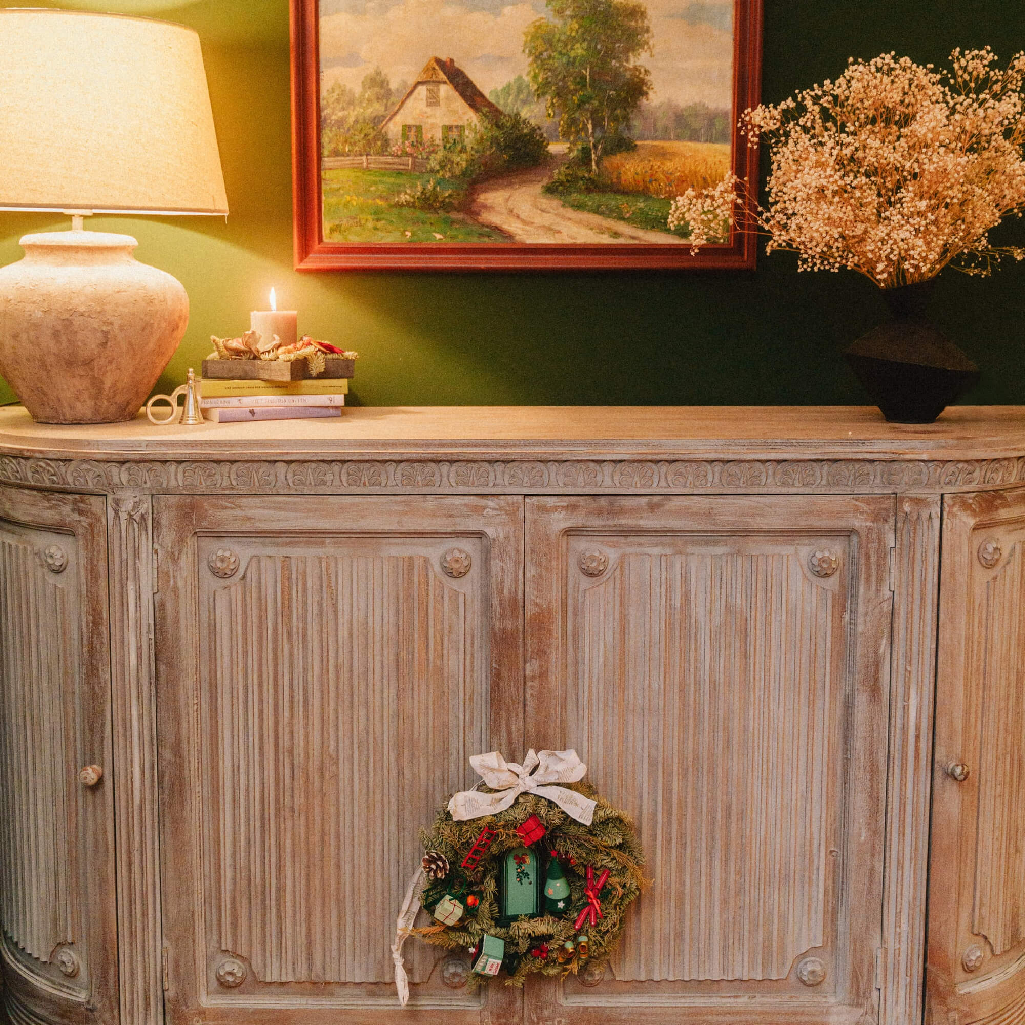 Rustieke houten dressoir met decoratieve krans en lamp tegen groene muur in gezellige woonkamer