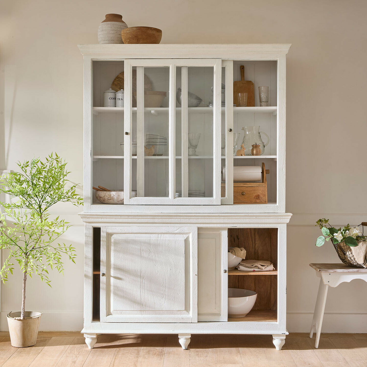 Witte houten kast met glazen deuren en planken voor servies in vintage stijl