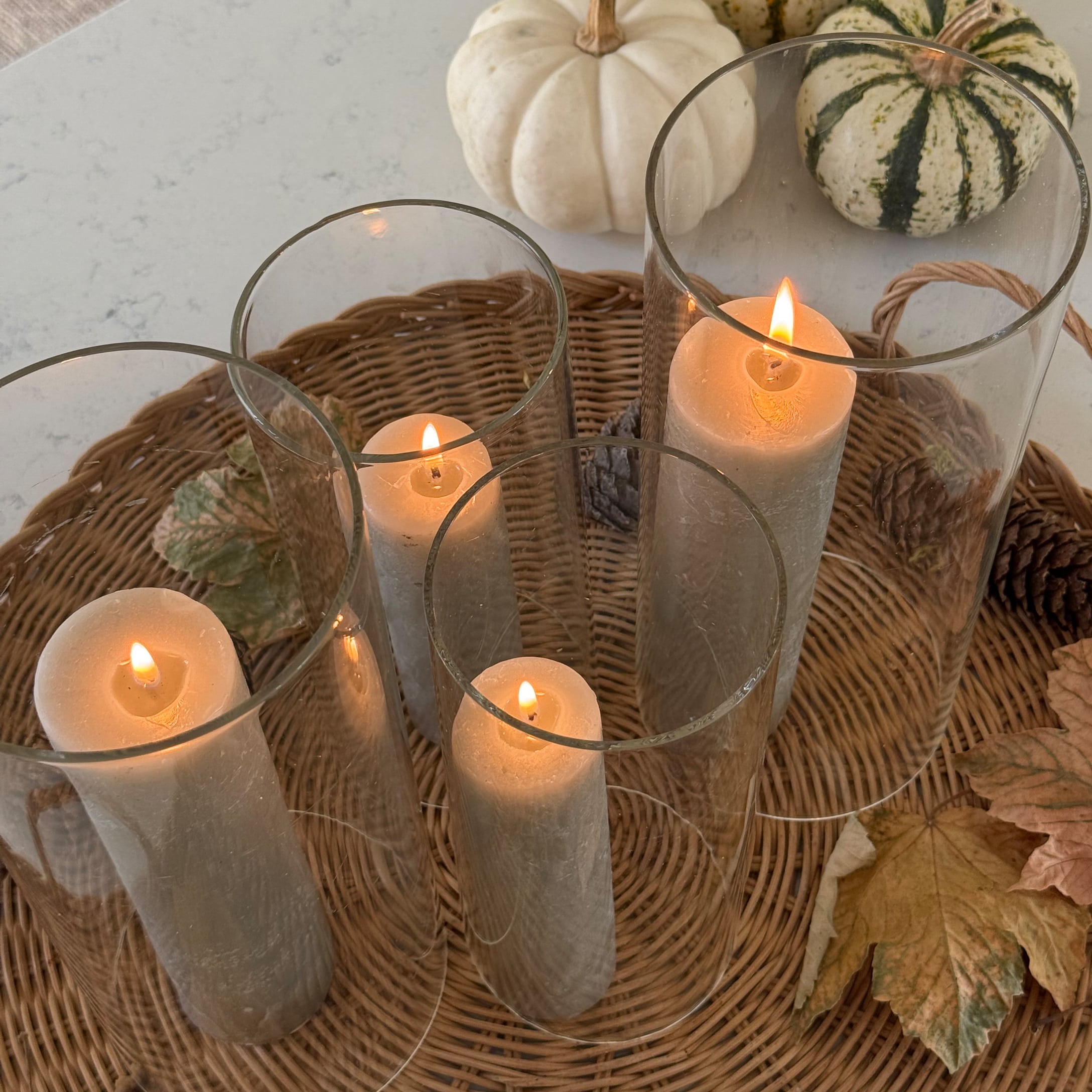 Set van vier witte kaarsen in glazen houders op een rieten dienblad met herfstdecoratie