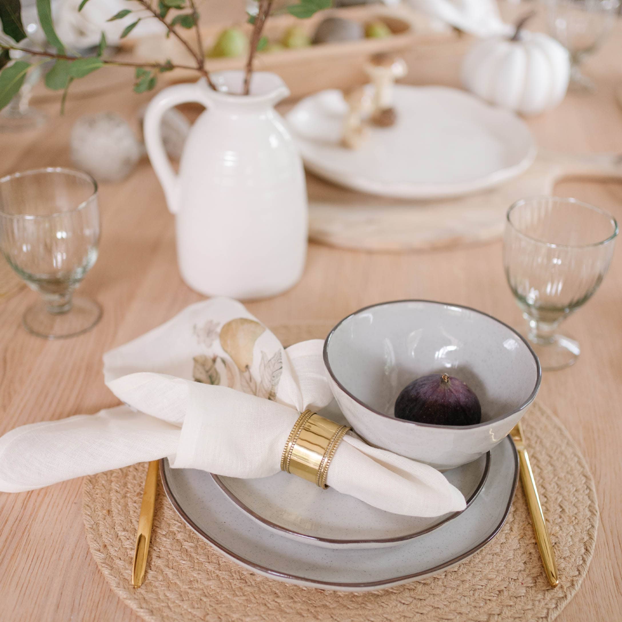 Tafelset van lichtgrijs keramiek met gouden bestek en linnen servet op natuurlijke placemat