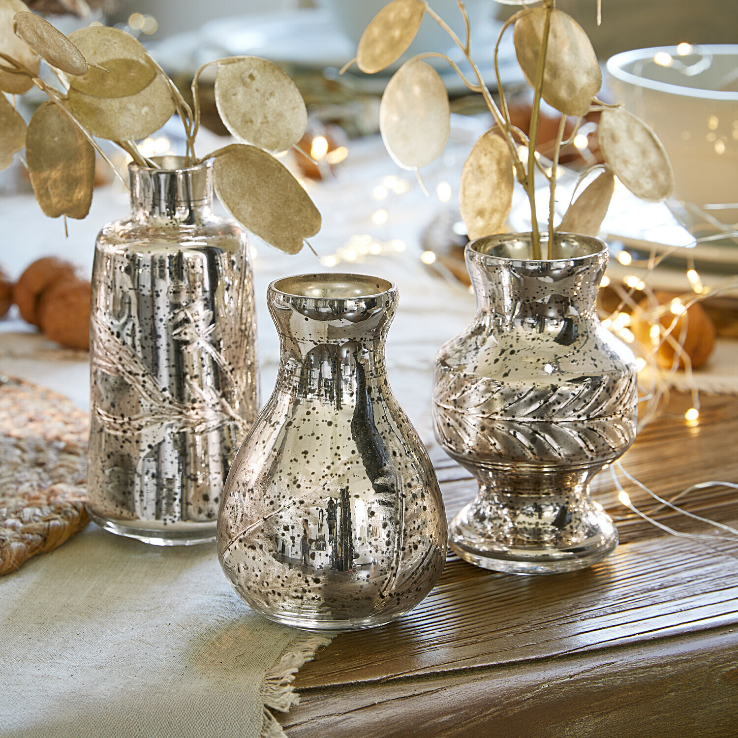 Set van drie zilverkleurige glazen vazen met decoratief bladmotief op een houten tafel