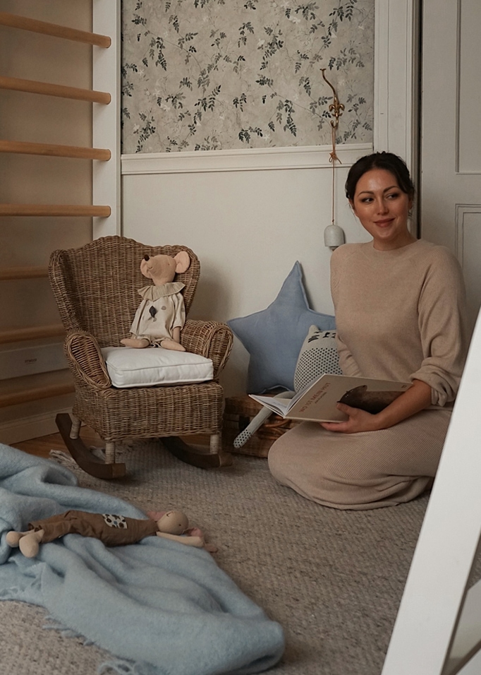 Gezellige kamer met rotan schommelstoel en knuffels op tapijt, vrouw leest boek.