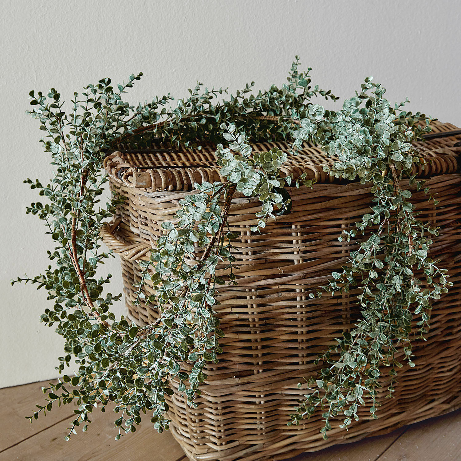 Guirlande Valerie Decoratieve krans van groene bladeren op een rieten mand op een houten vloer