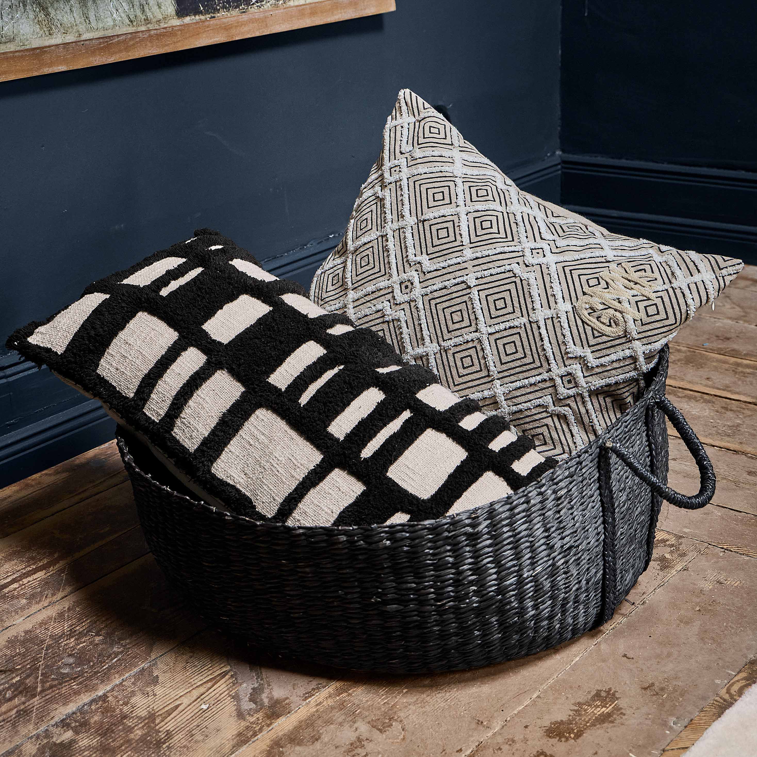 Zwart-witte decoratieve kussen met geometrisch patroon in mand op houten vloer