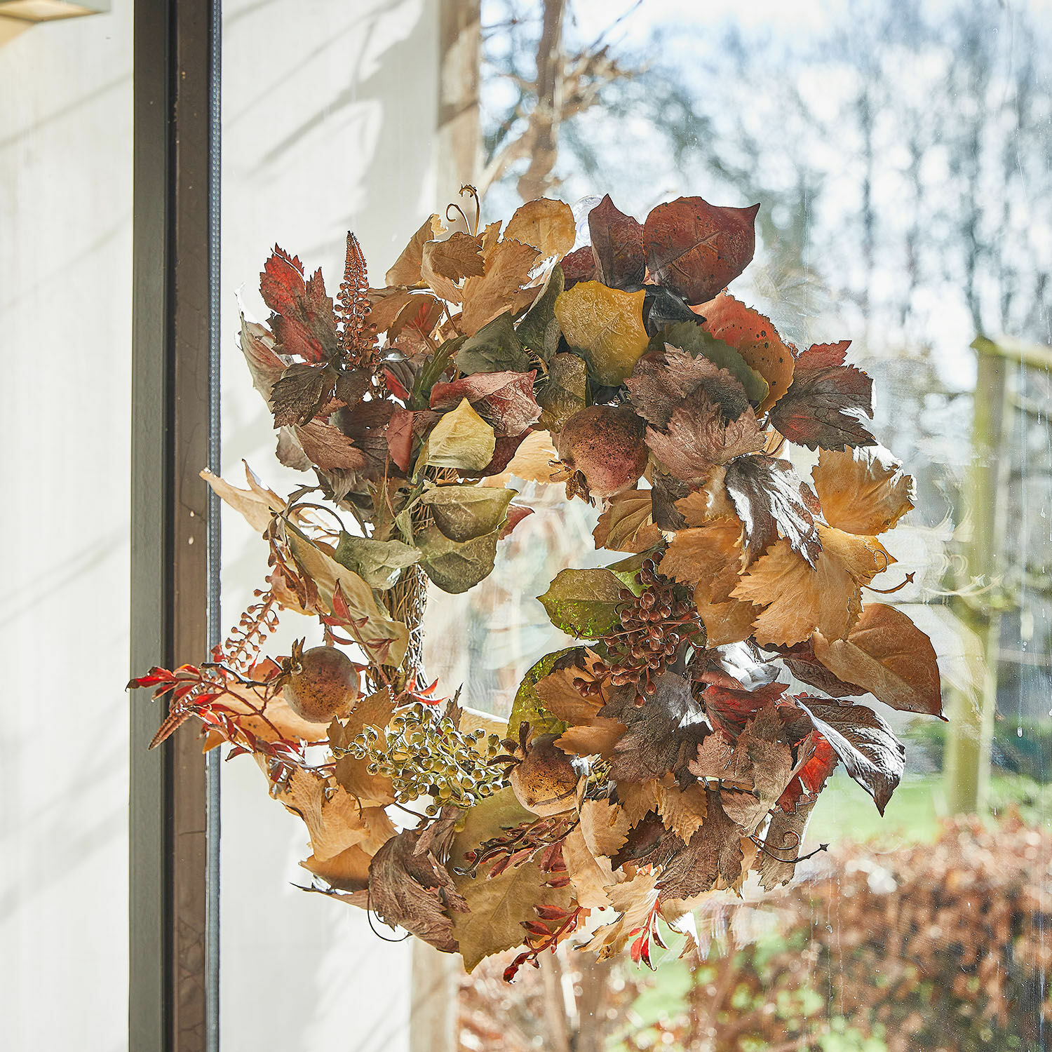Herfstkrans van gedroogde bladeren en vruchten in natuurlijke bruine tinten voor deur of raam